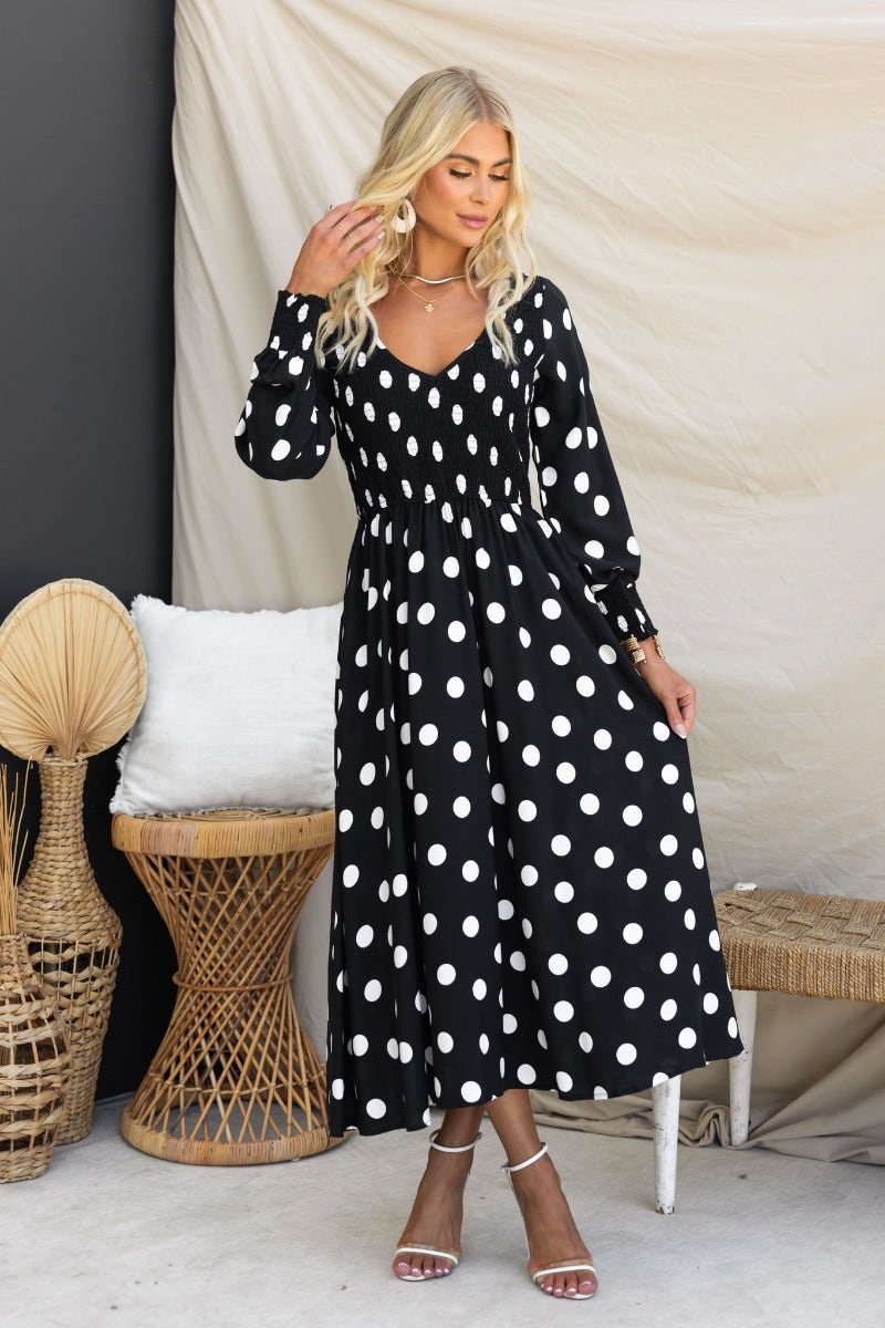 Black polka dot midi dress with V-neckline and puff sleeves, featuring relaxed fit and elasticated bodice.