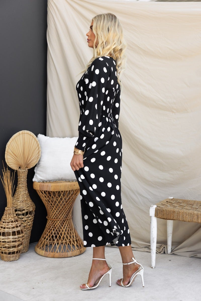Dostan Midi Dress: Black polka dot dress with V-neckline and elastic details, styled with heels.