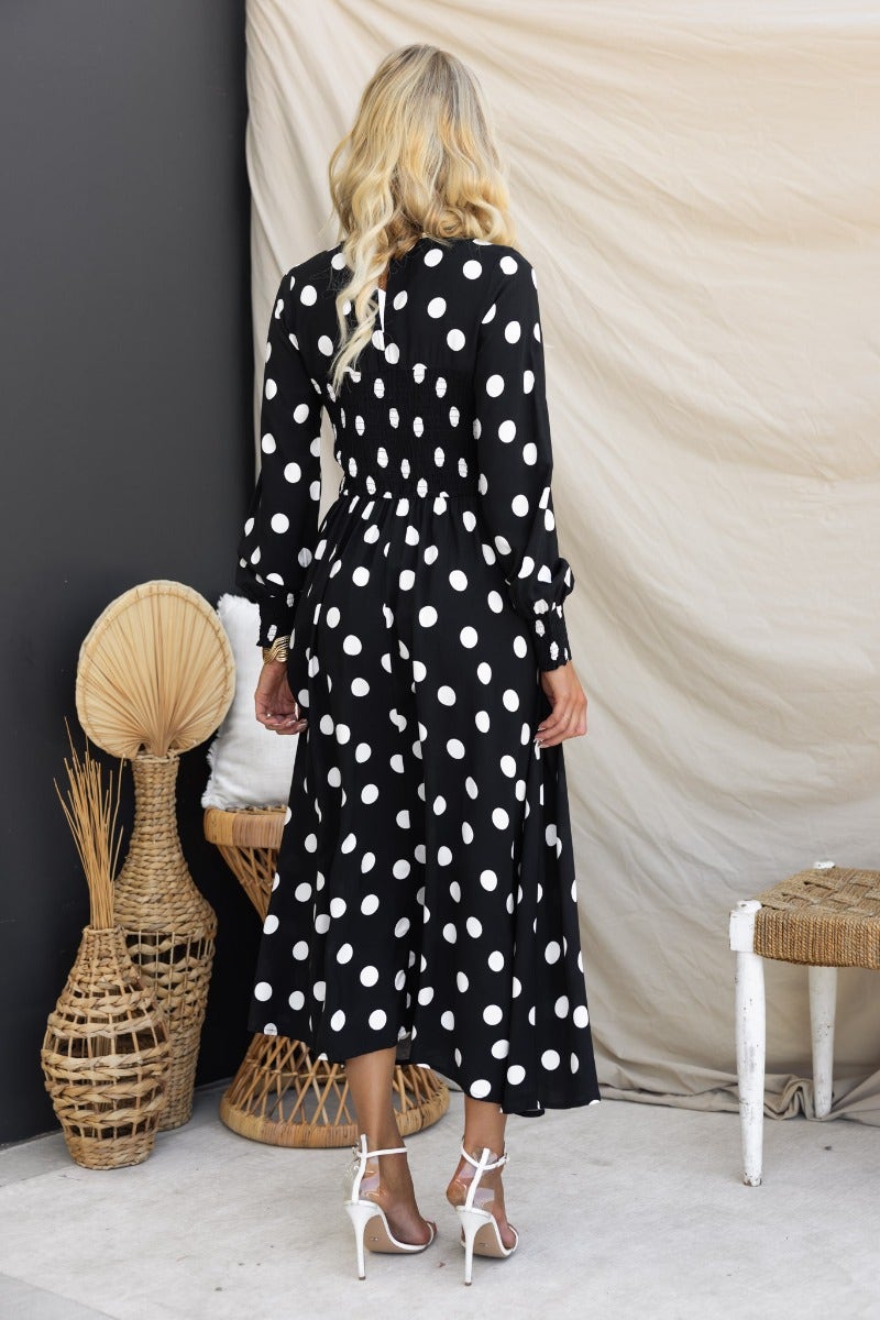 Model wearing a black polka dot midi dress, featuring a V-neckline and elastic cuffs, set against a neutral background.
