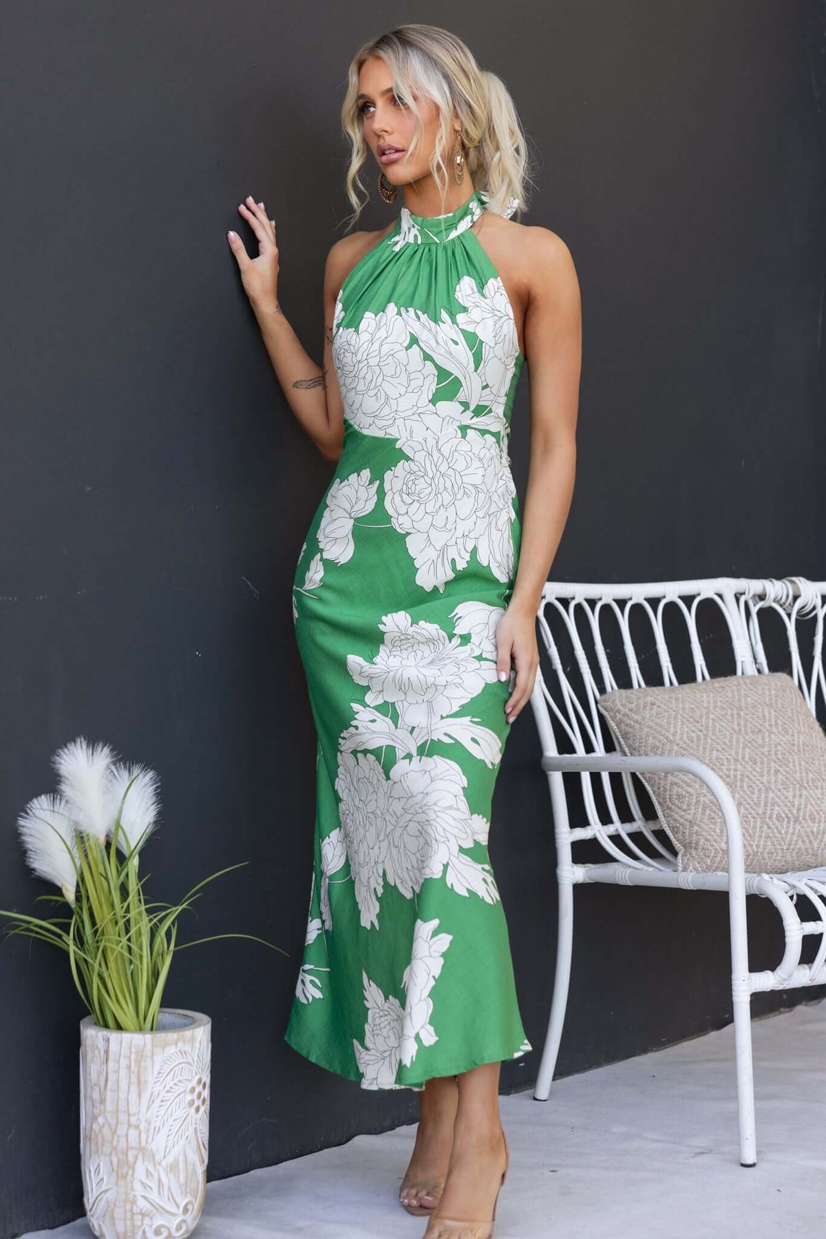 Model wearing a green floral maxi dress with high tie neckline, showcasing elegant design and fitted silhouette.