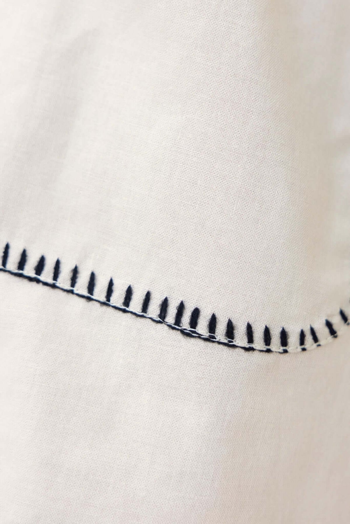 Close-up of detailed stitching on light fabric, showcasing craftsmanship and texture in a linen-like material.