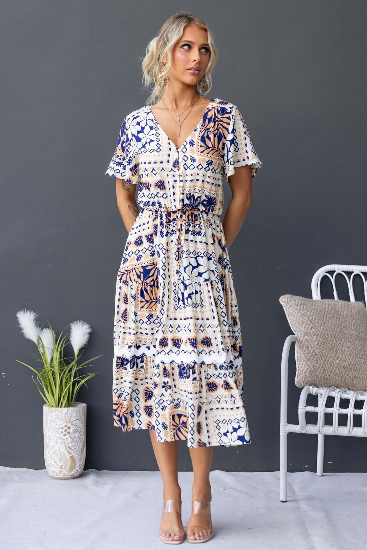 Virden Midi Dress featuring a V-neckline, button-up bust, pockets, and a relaxed fit, styled with a potted plant.