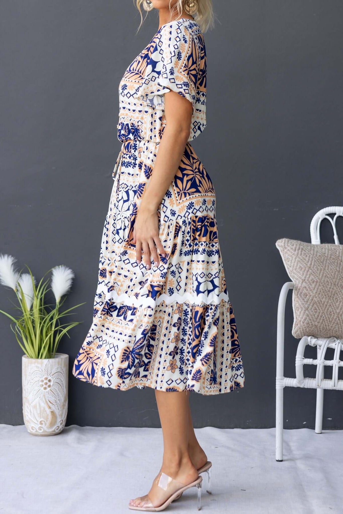 Side view of a woman in a stylish Virden Midi Dress with a floral print, featuring a V-neckline and elastic waistband.