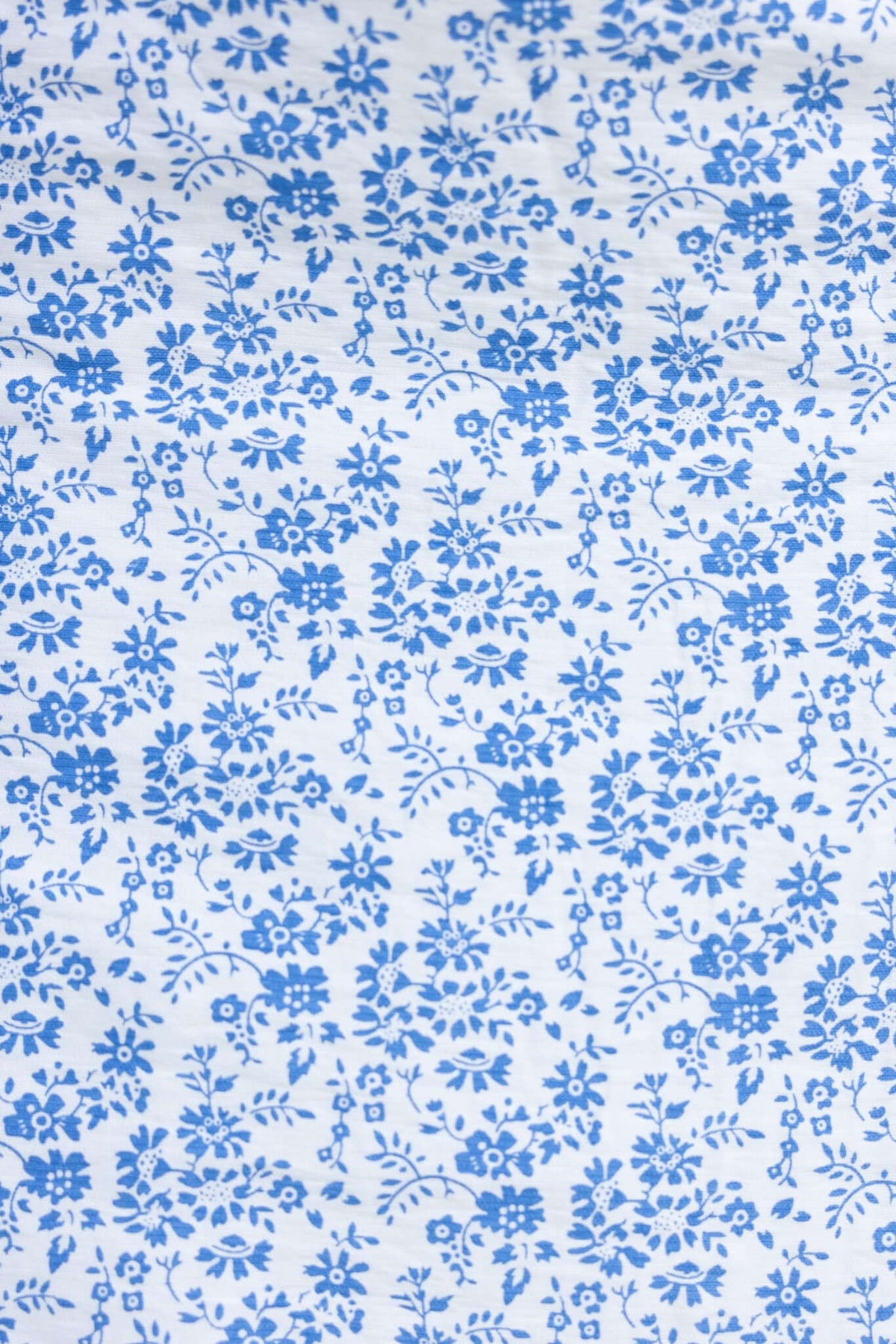 Blue floral pattern fabric with intricate designs on a light background, ideal for clothing and textile projects.