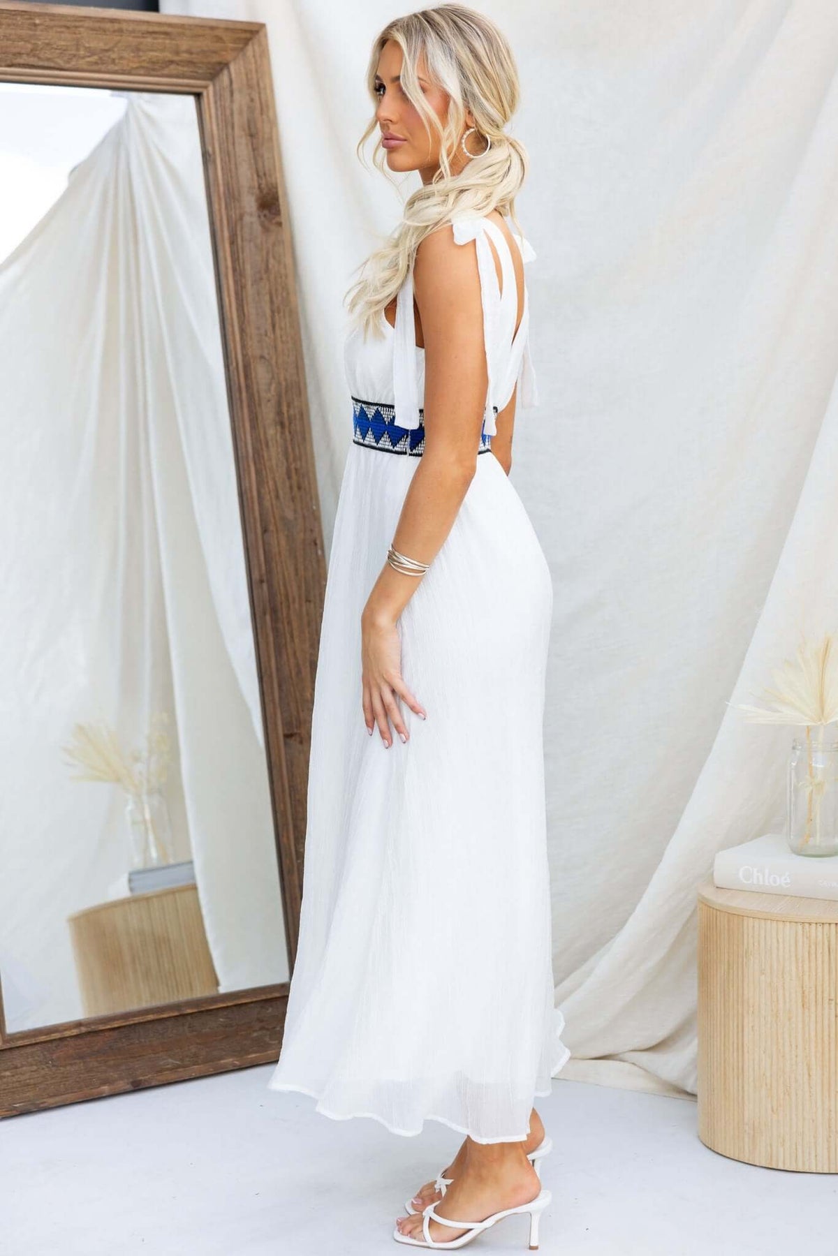 Woman wearing white Egret Maxi Dress with tie straps and elastic waistband, posing by a mirror.