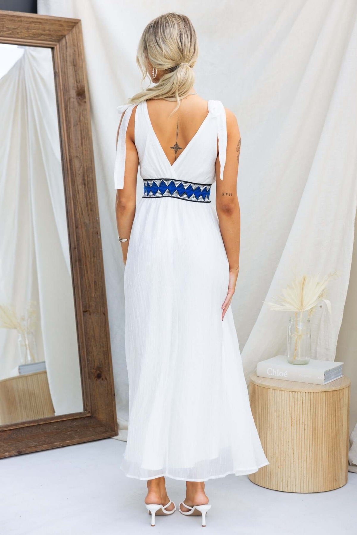 Back view of a woman wearing a white Egret maxi dress with tie straps and colorful waist detail.
