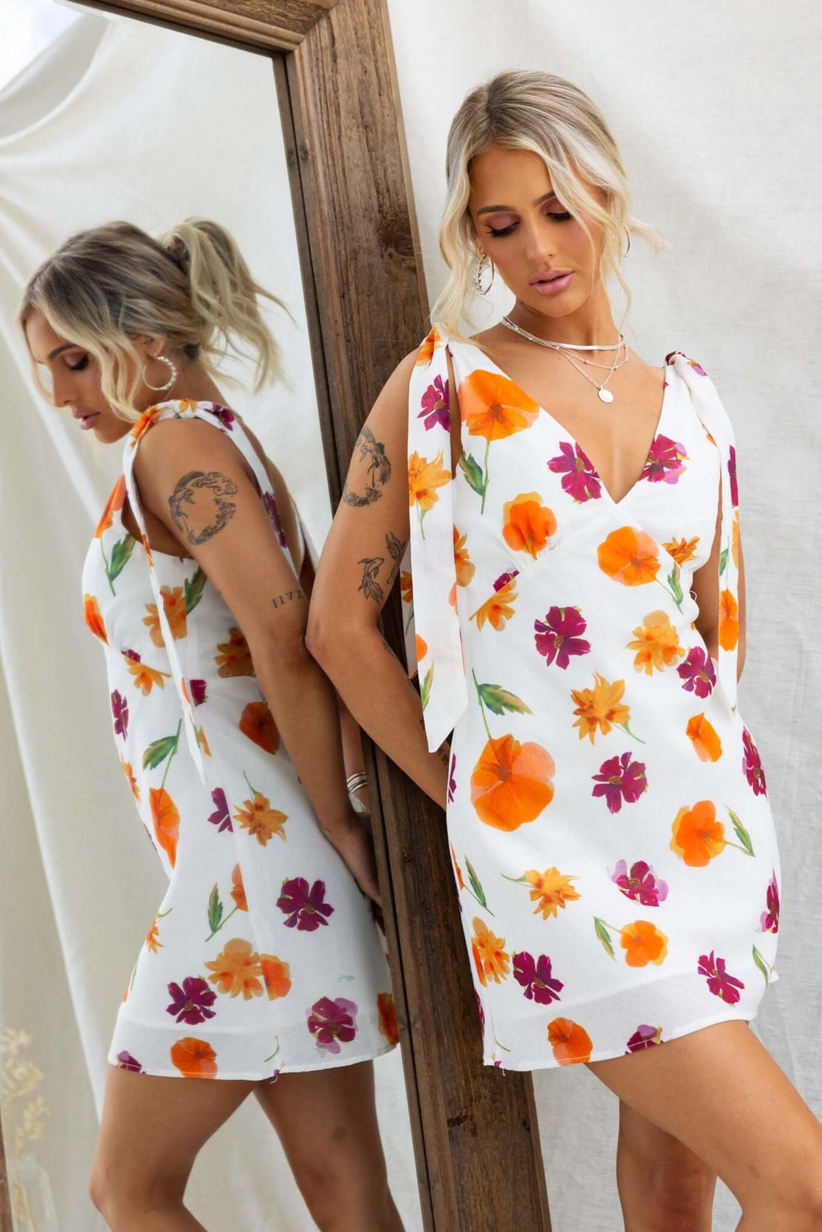 Floral print Kinsey dress with adjustable tie straps, modeled by a woman in front of a mirror.