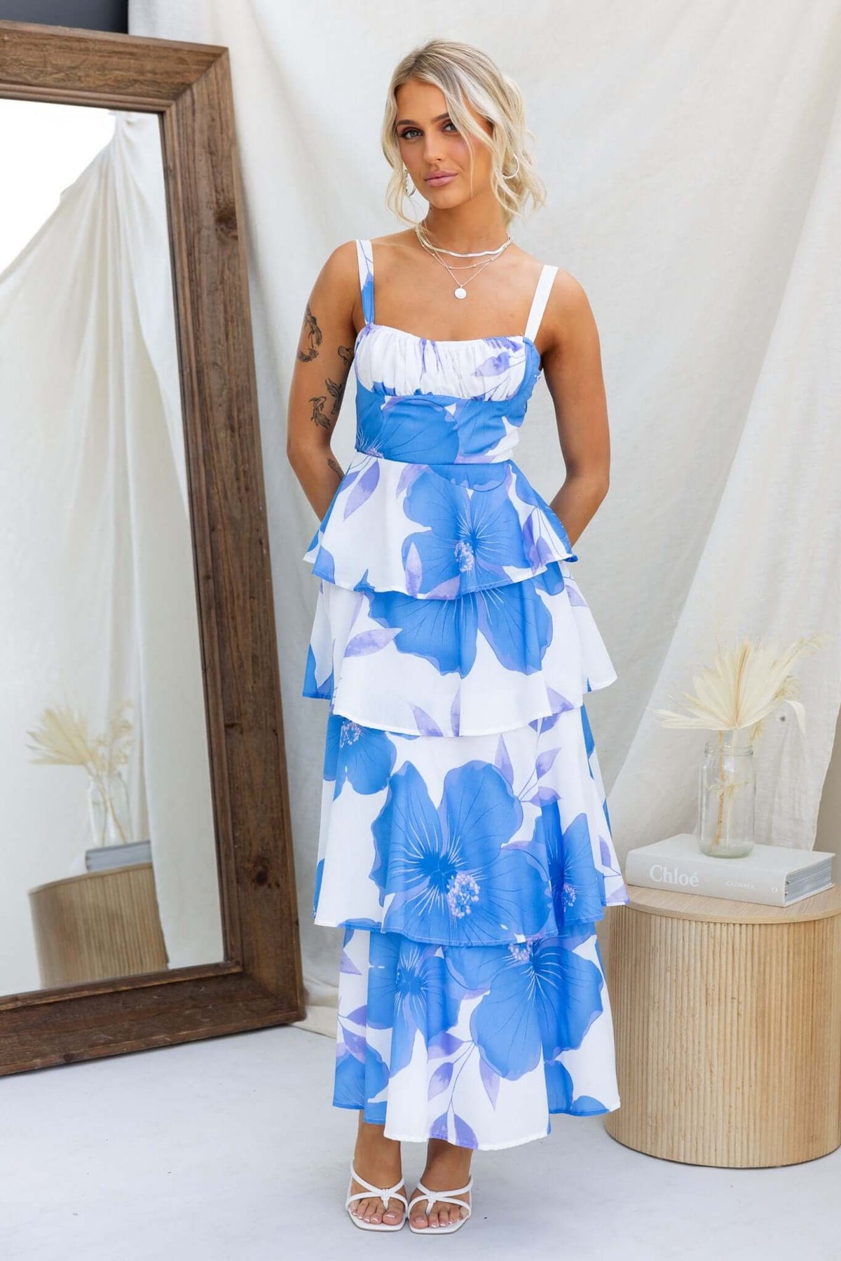 Peyton Maxi Dress with adjustable straps and multi-tier ruffle skirt in blue floral design, styled against a mirror backdrop.