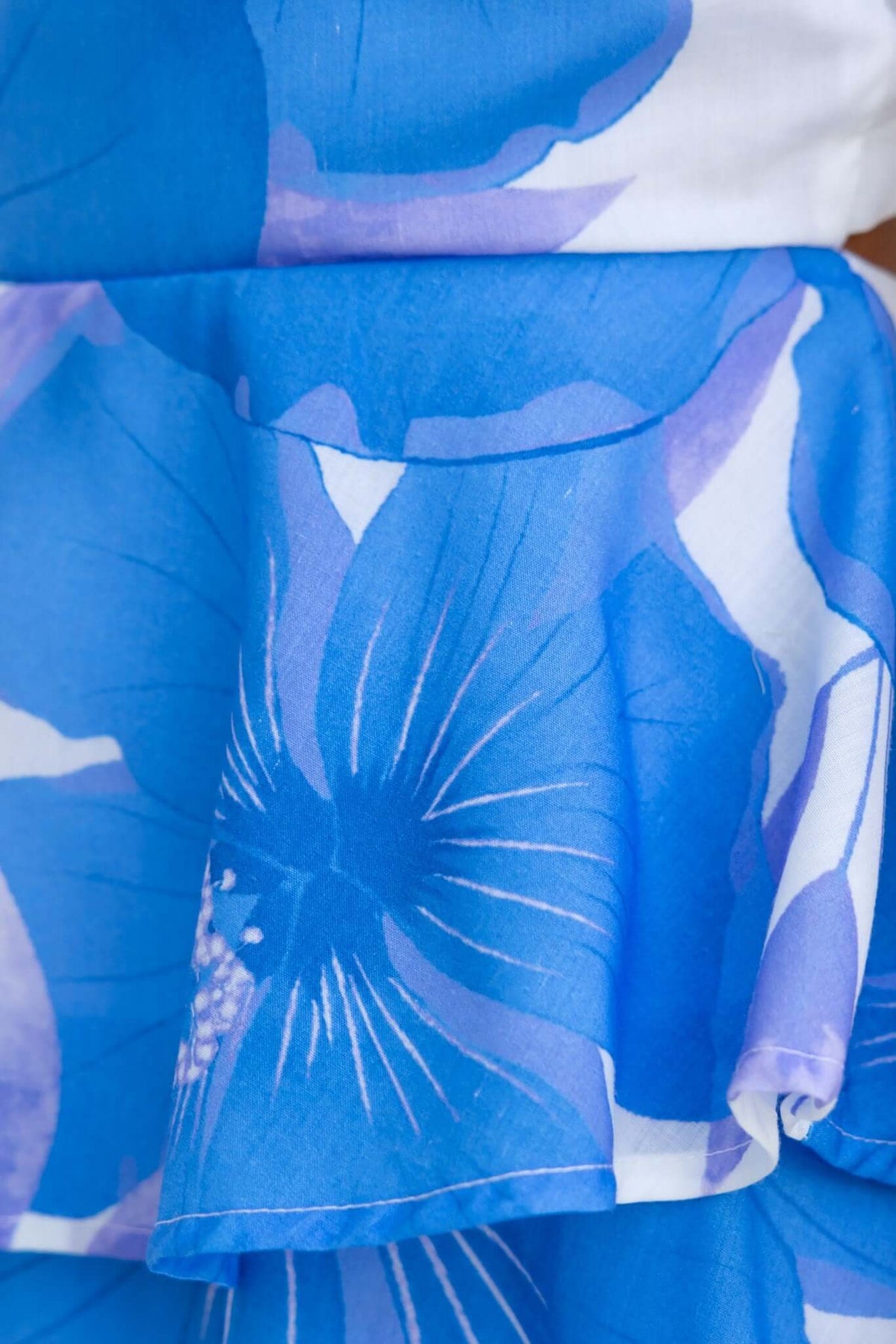 Close-up of blue floral fabric with ruffle detailing on a maxi dress, showcasing vibrant floral patterns.