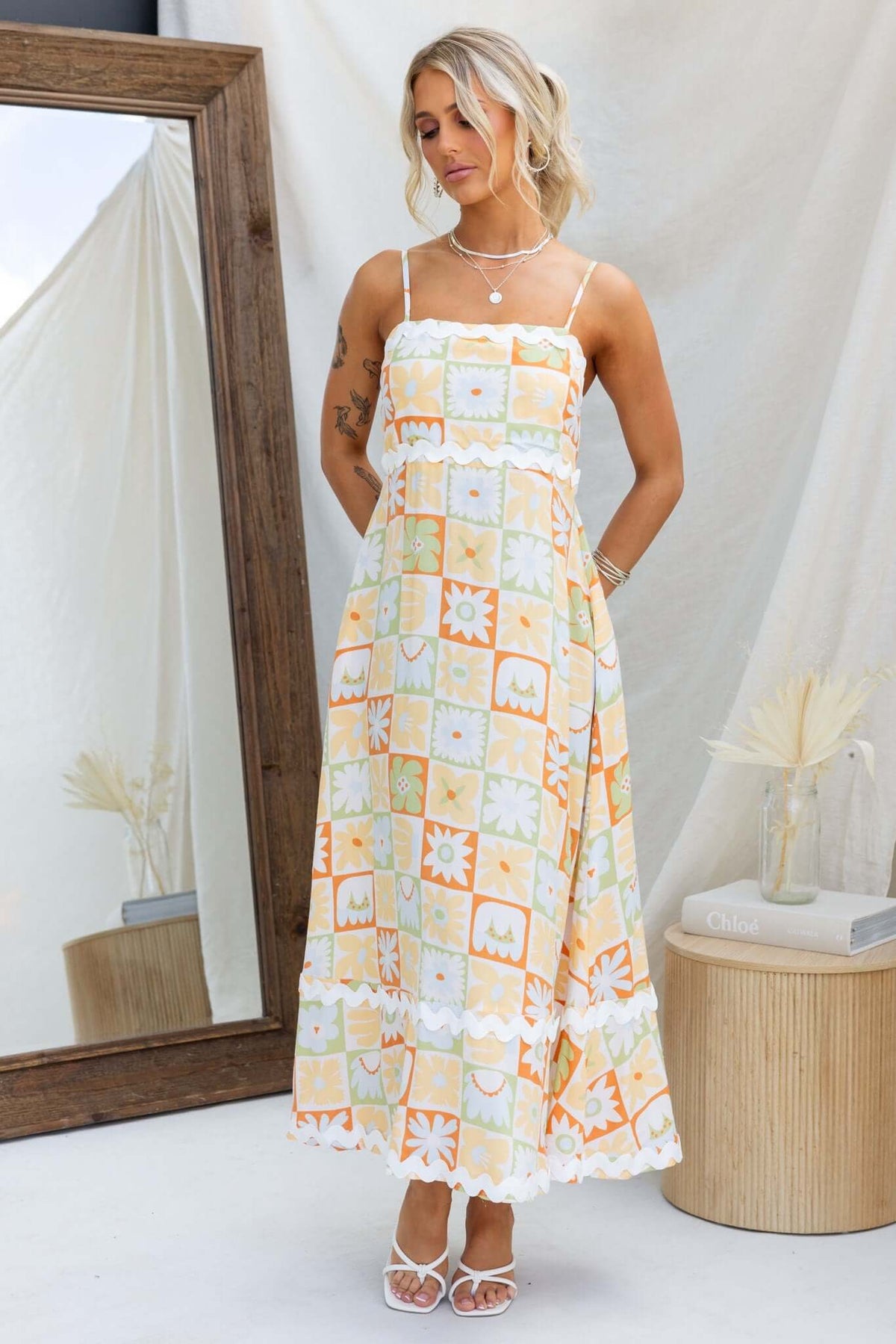 Nekoda Midi Dress with adjustable straps, pockets, and a vibrant floral pattern, worn by a model in a styled setting.