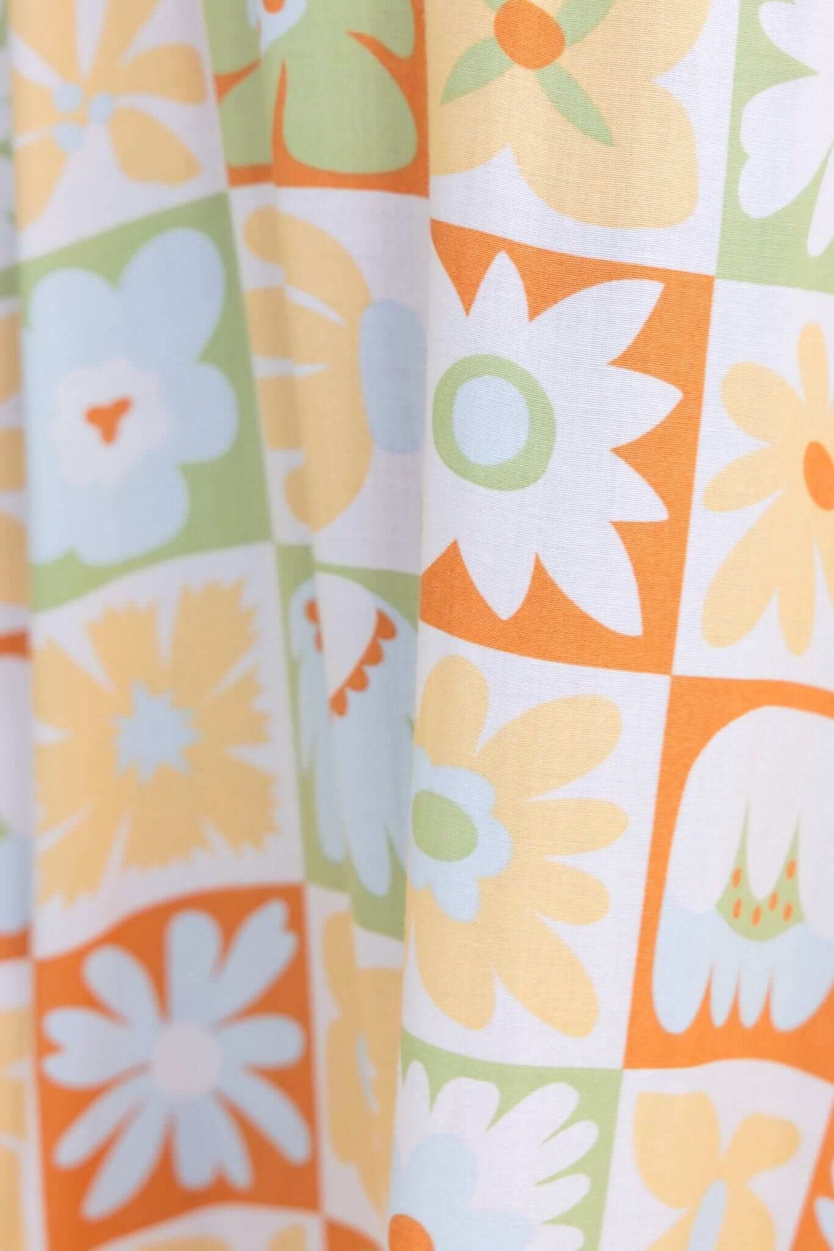 Close-up of colorful floral patterned fabric featuring orange, yellow, blue, and green designs in a grid layout.