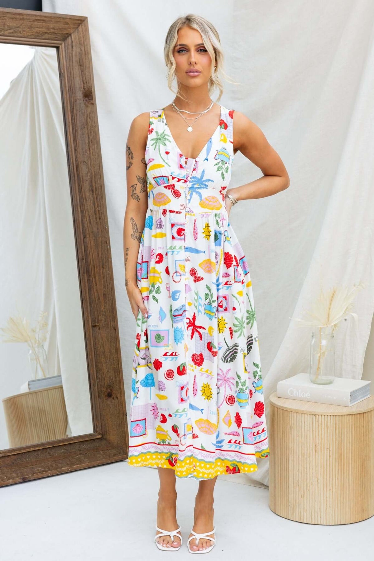 Model wearing Juvena Midi Dress with colorful patterns, featuring a V-neckline and button-up front, in a bright, airy setting.