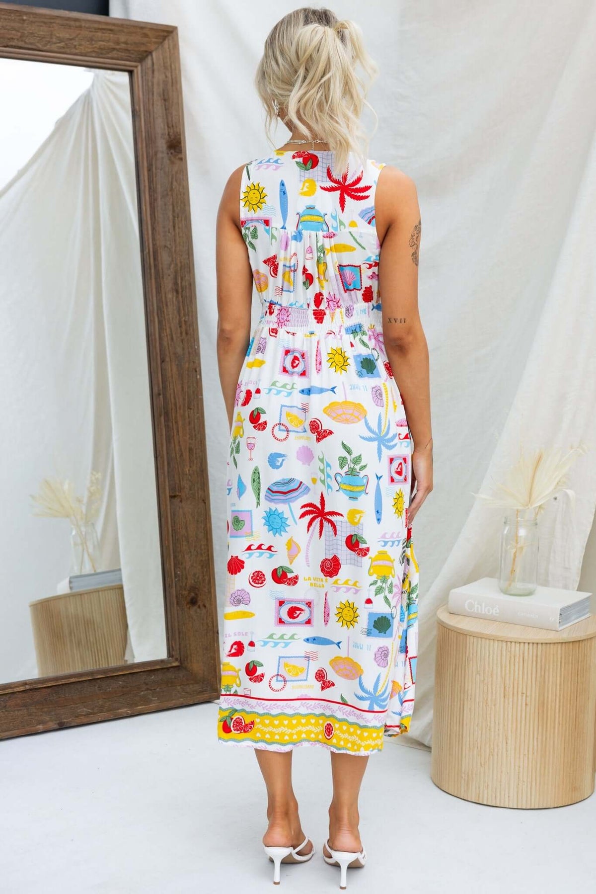 Back view of a colorful Juvena midi dress featuring a vibrant print, V-neckline and elastic at back, styled with sandals.