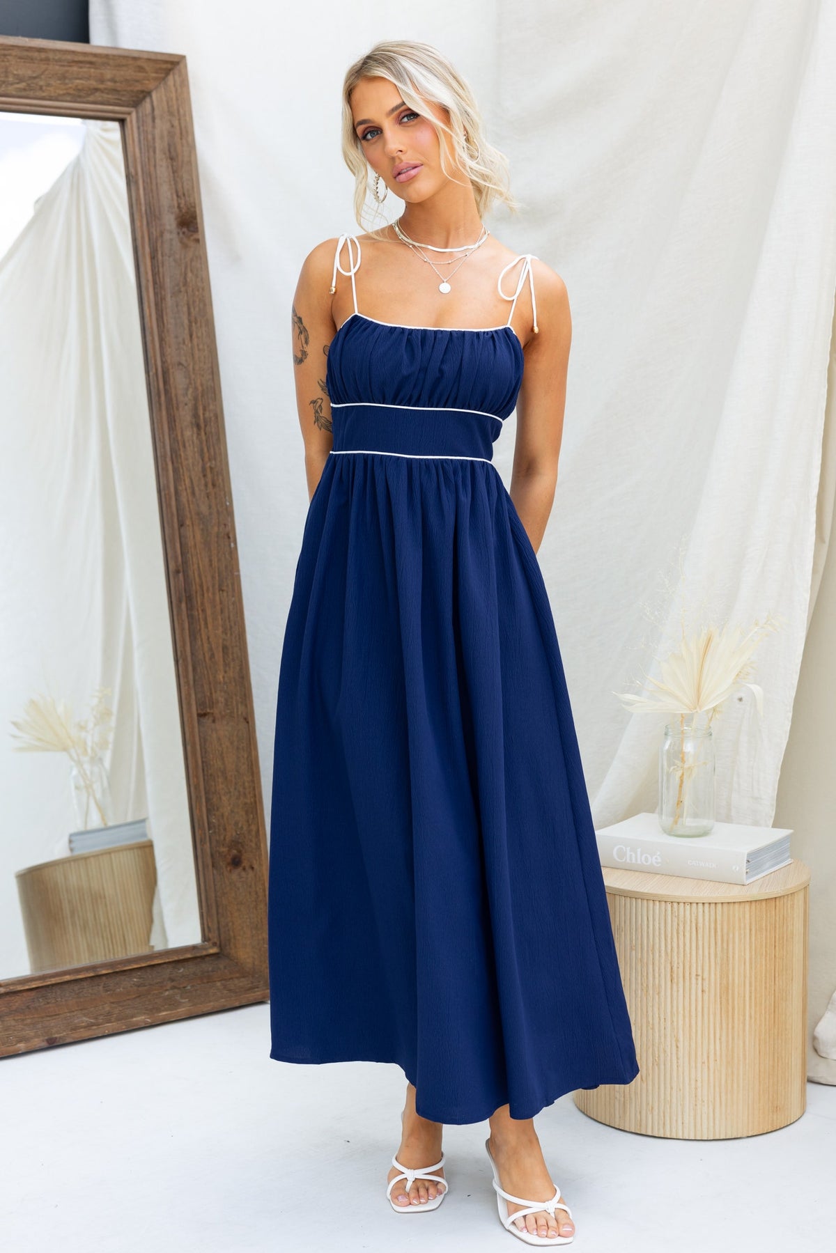Navy Genessa Midi Dress with tie straps, featuring an elastic back and lined design, styled in a chic setting.