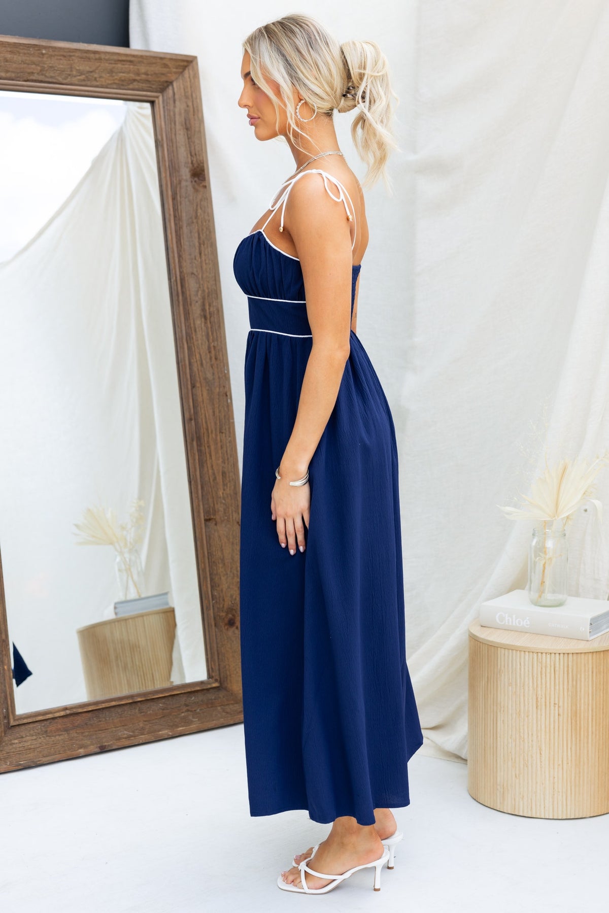 Side view of the Genessa Midi Dress in navy with tie straps and elastic back, styled with white sandals.