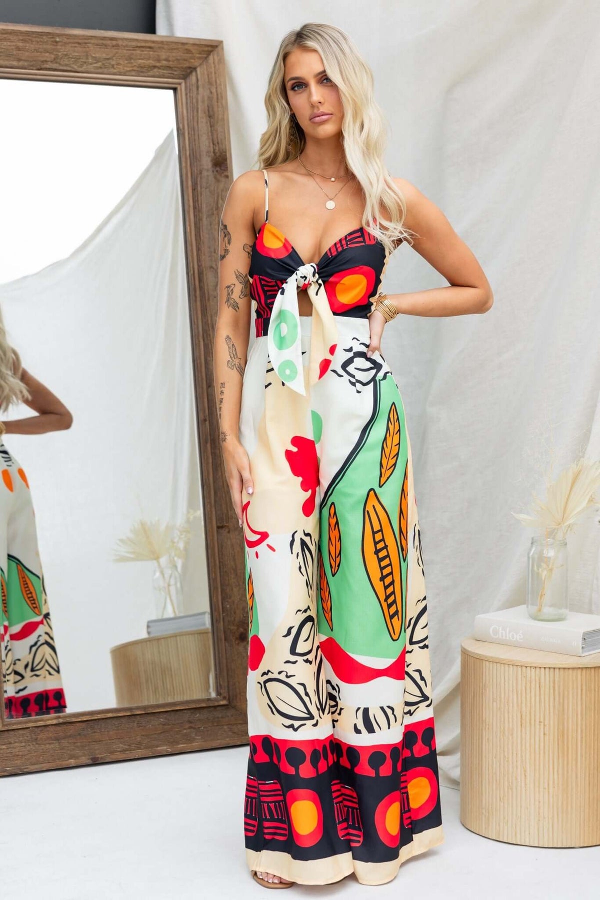 Sun Dazed Jumpsuit featuring a colorful print, adjustable straps, and a tie at the bust, styled with pockets.