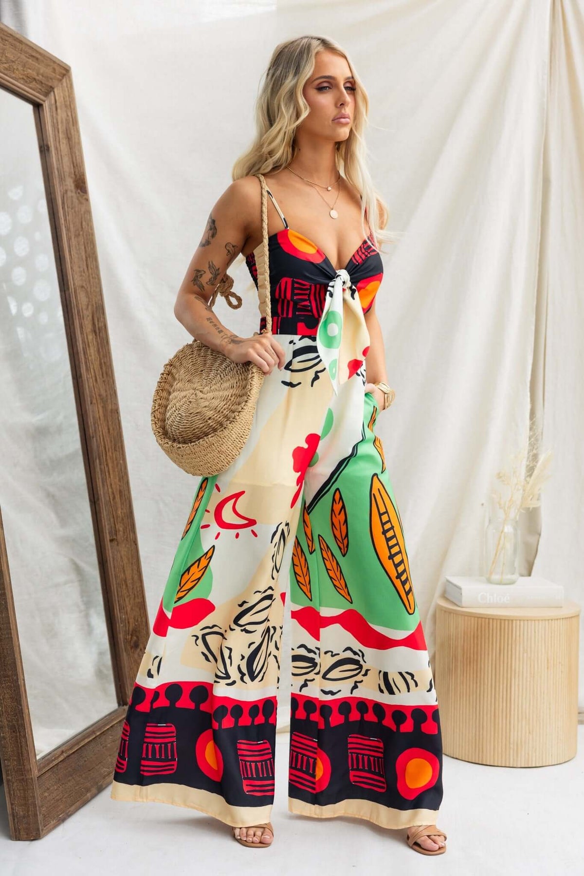 Model wearing a multi-colour print Sun Dazed Jumpsuit with adjustable straps and tie detail.