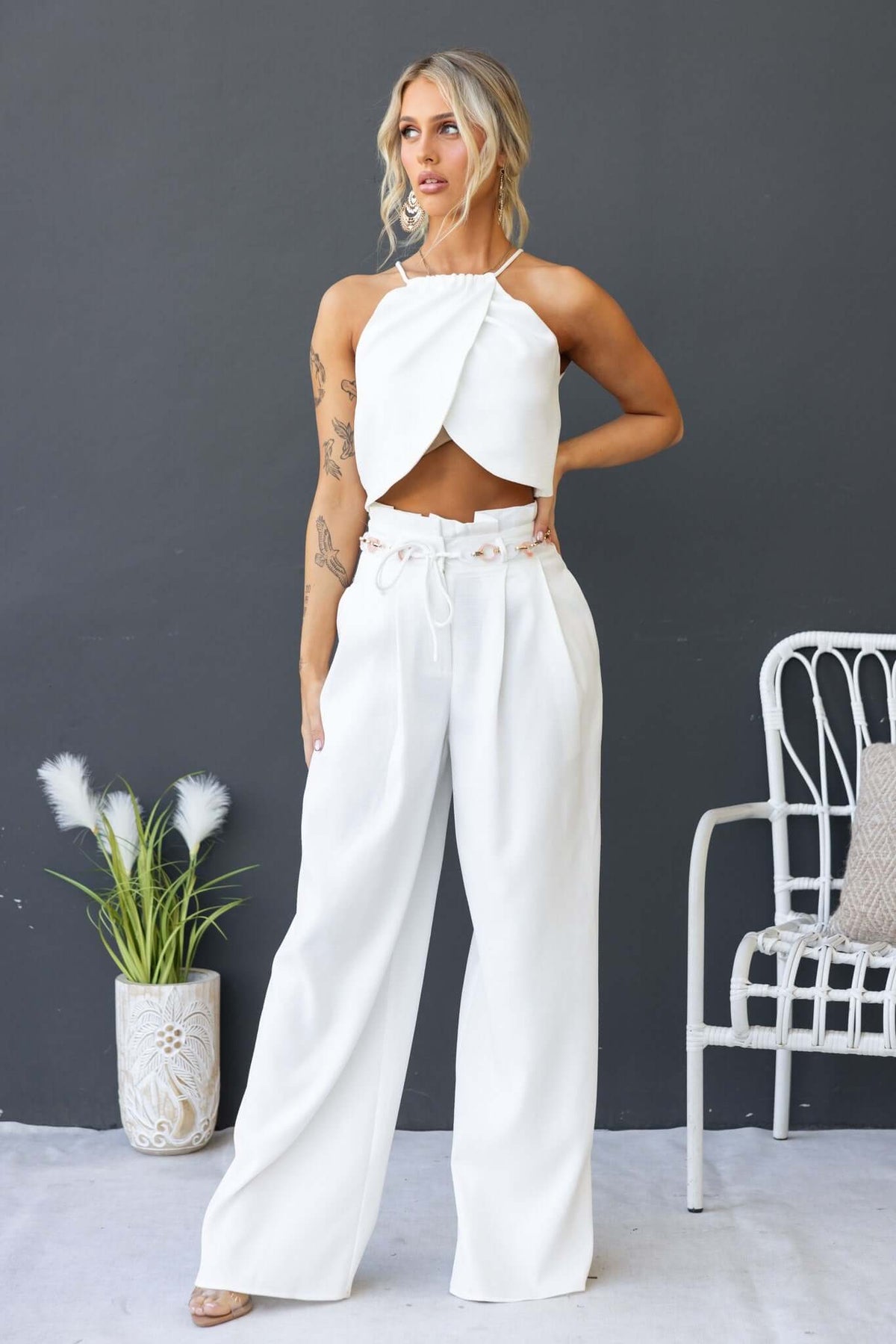 Model wearing a stylish white Paytas top with high neckline, paired with wide-leg pants, set against a neutral background.