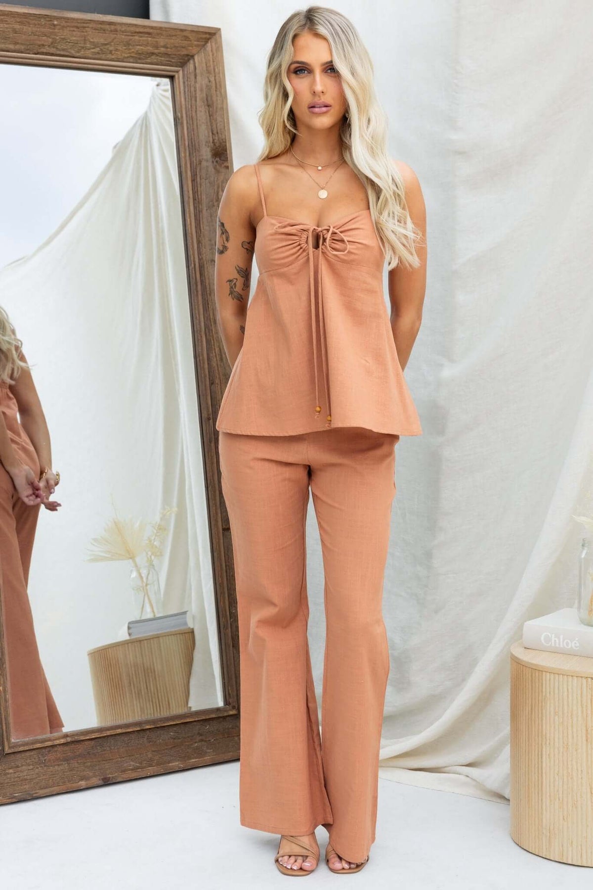 Model wearing a stylish Stelline Top with adjustable straps and tie at bust, paired with matching pants against a neutral backdrop.