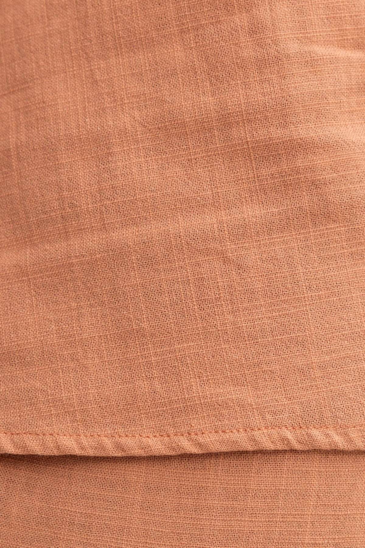 Close-up of textured linen look fabric in warm coral color, showcasing soft, lightweight material.