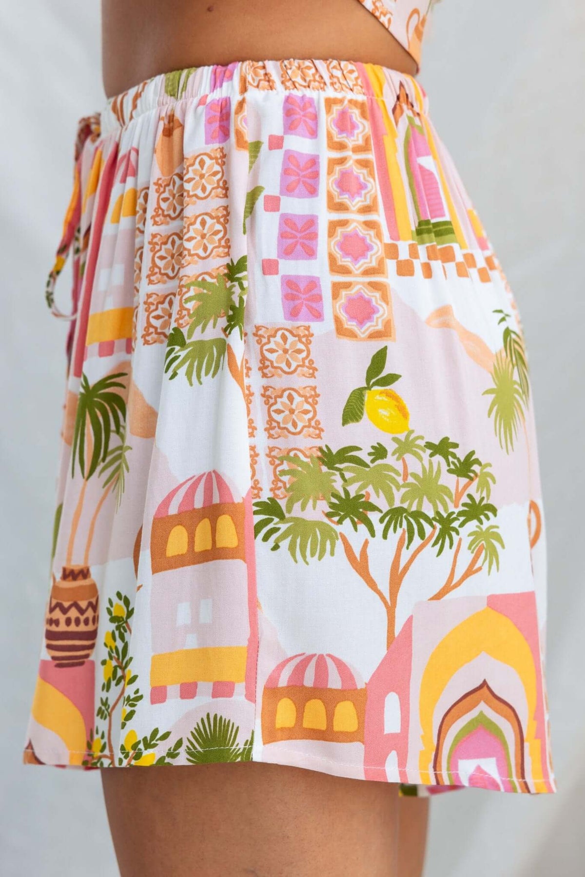 Junia Set shorts featuring vibrant print with palm trees and colorful buildings, showcasing mid-high waist and drawstring.