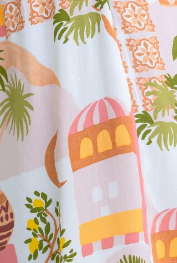 Colorful fabric pattern featuring palm trees and decorative buildings, ideal for the Junia Set shirt and shorts.