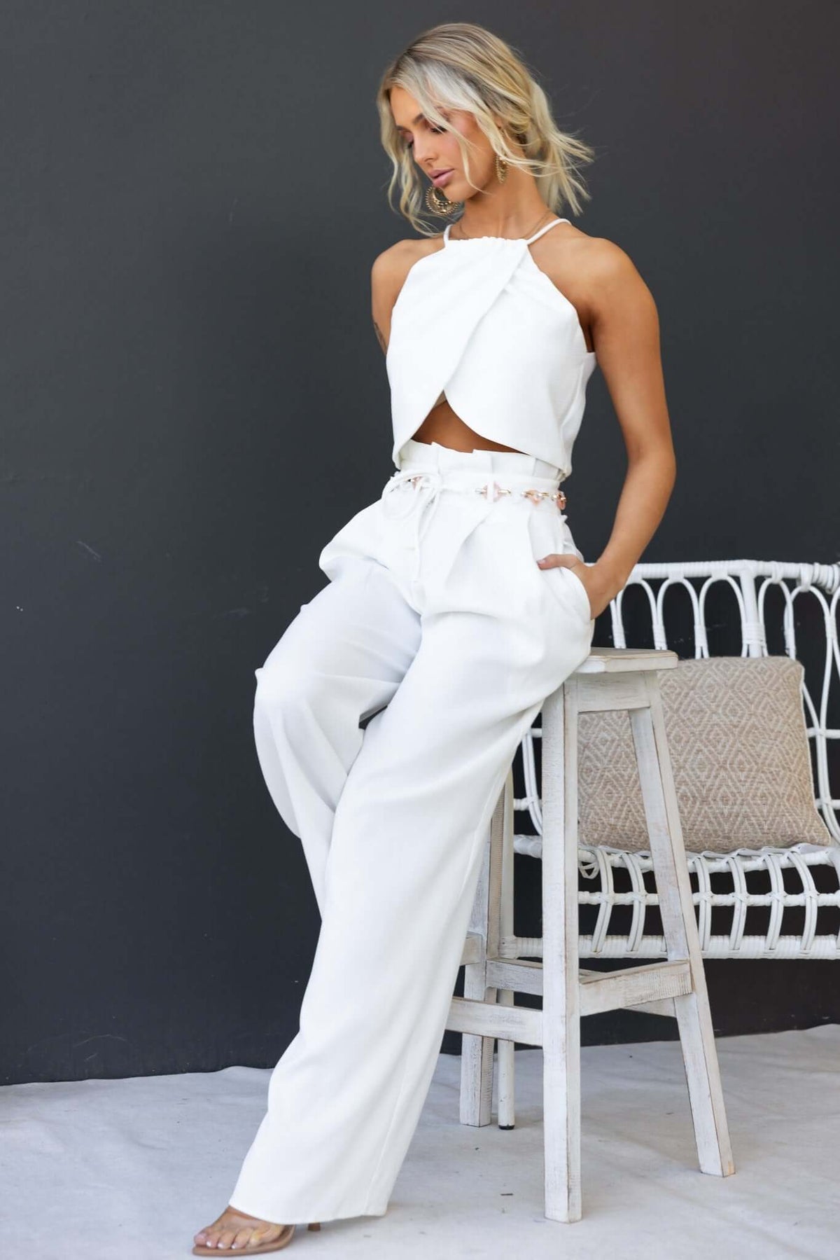 Model wearing Paytas Pants with paperbag waist and removable belt, styled with a chic top, posing by a white chair.