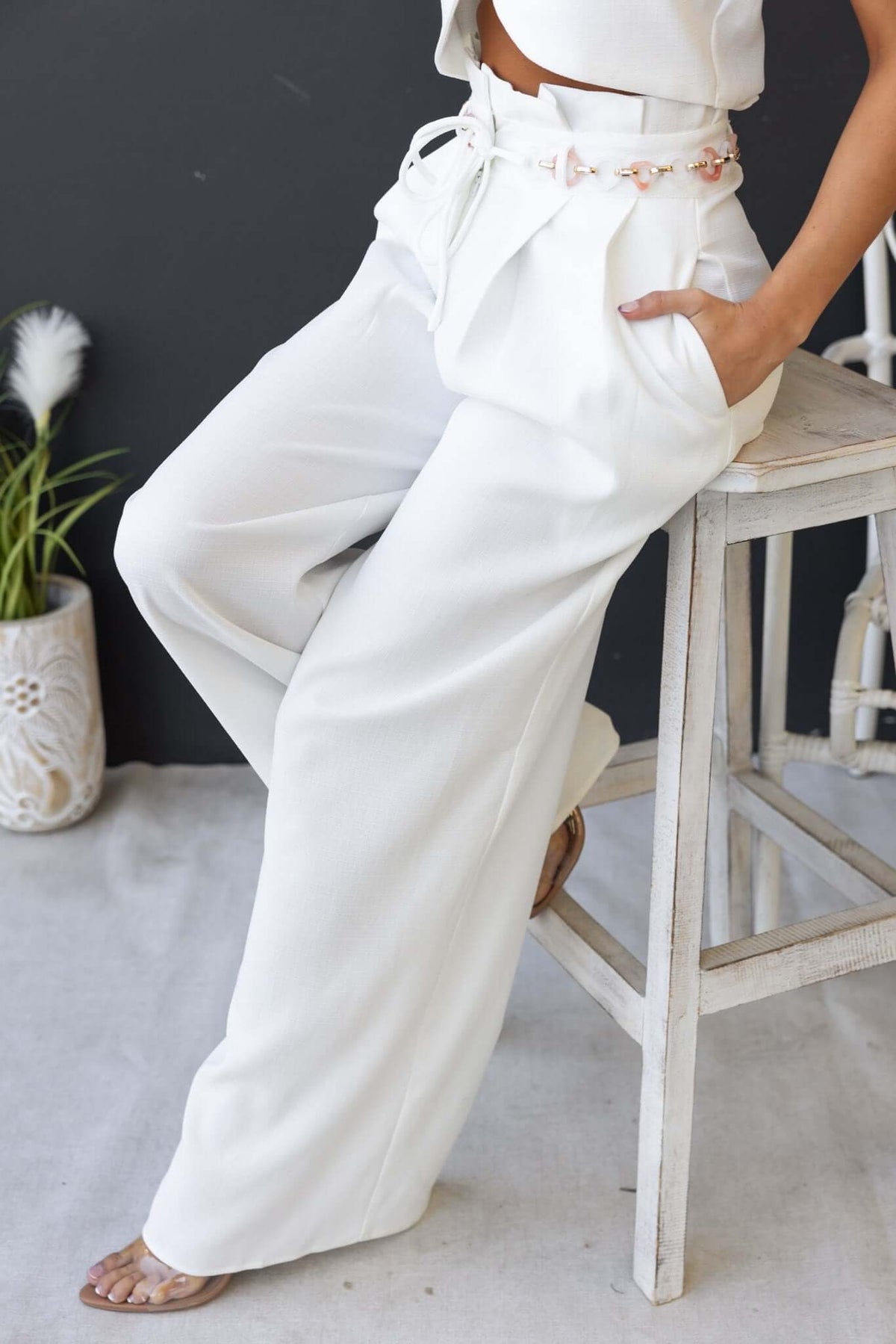 White paperbag waist pants with removable belt and pockets, styled for a casual look.