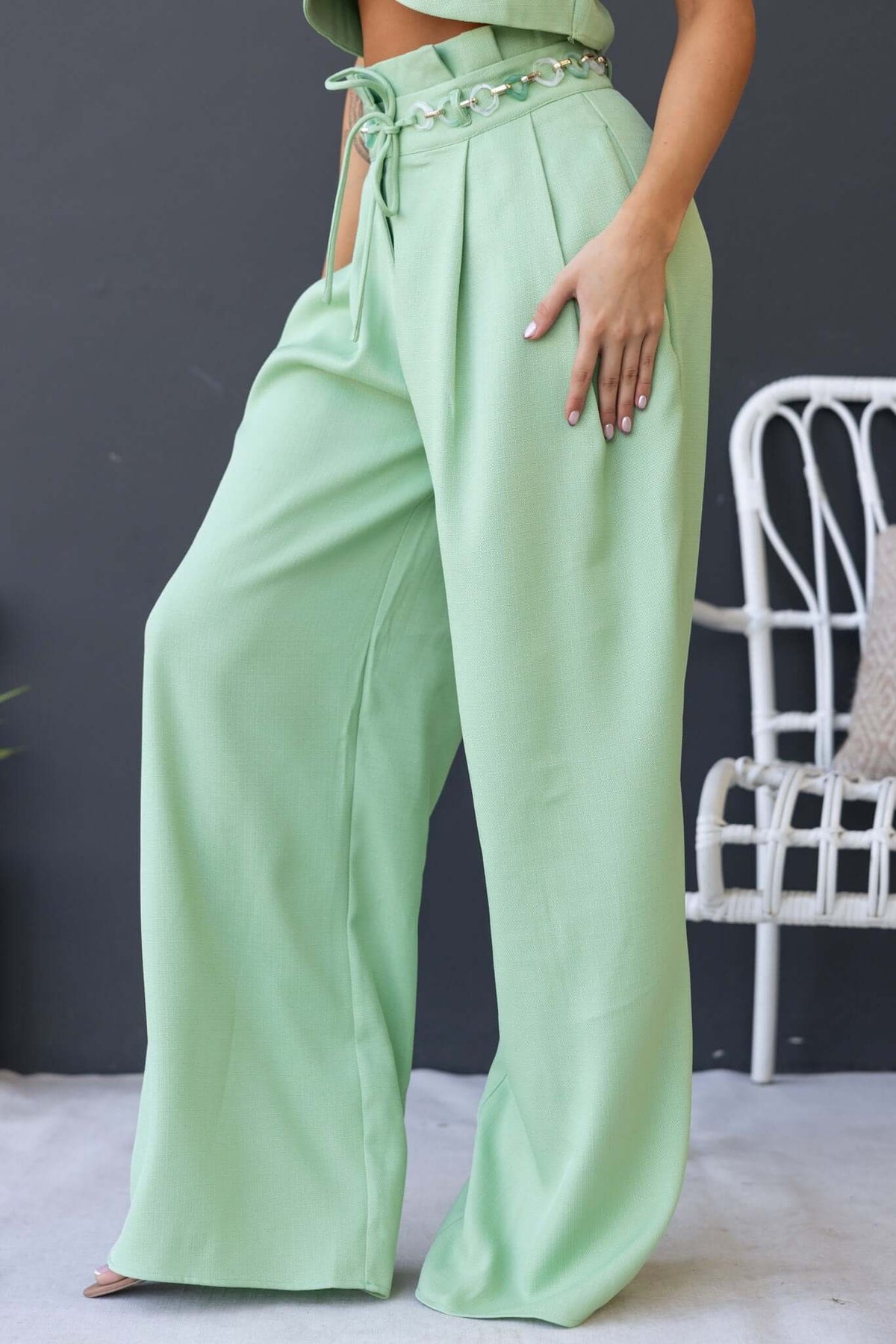 Green paperbag waist pants featuring removable belt and pockets, styled for a fashion-forward look.
