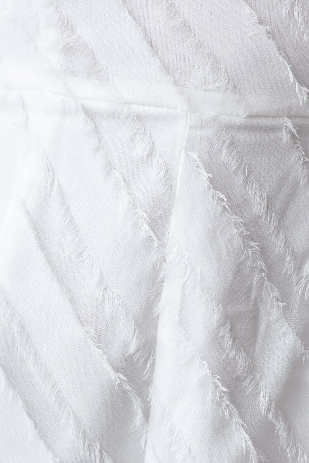 Close-up of textured white fabric with diagonal frayed patterns, showcasing the material of the Bossier Playsuit.