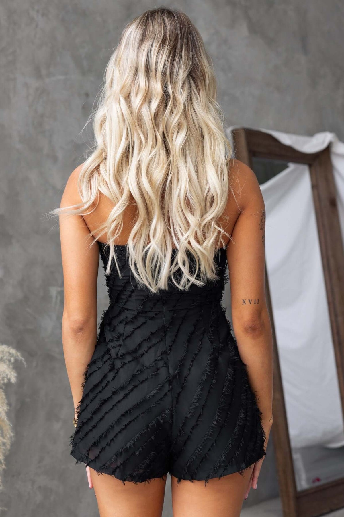Back view of a woman in a black strapless Bossier playsuit with textured material and lined design.