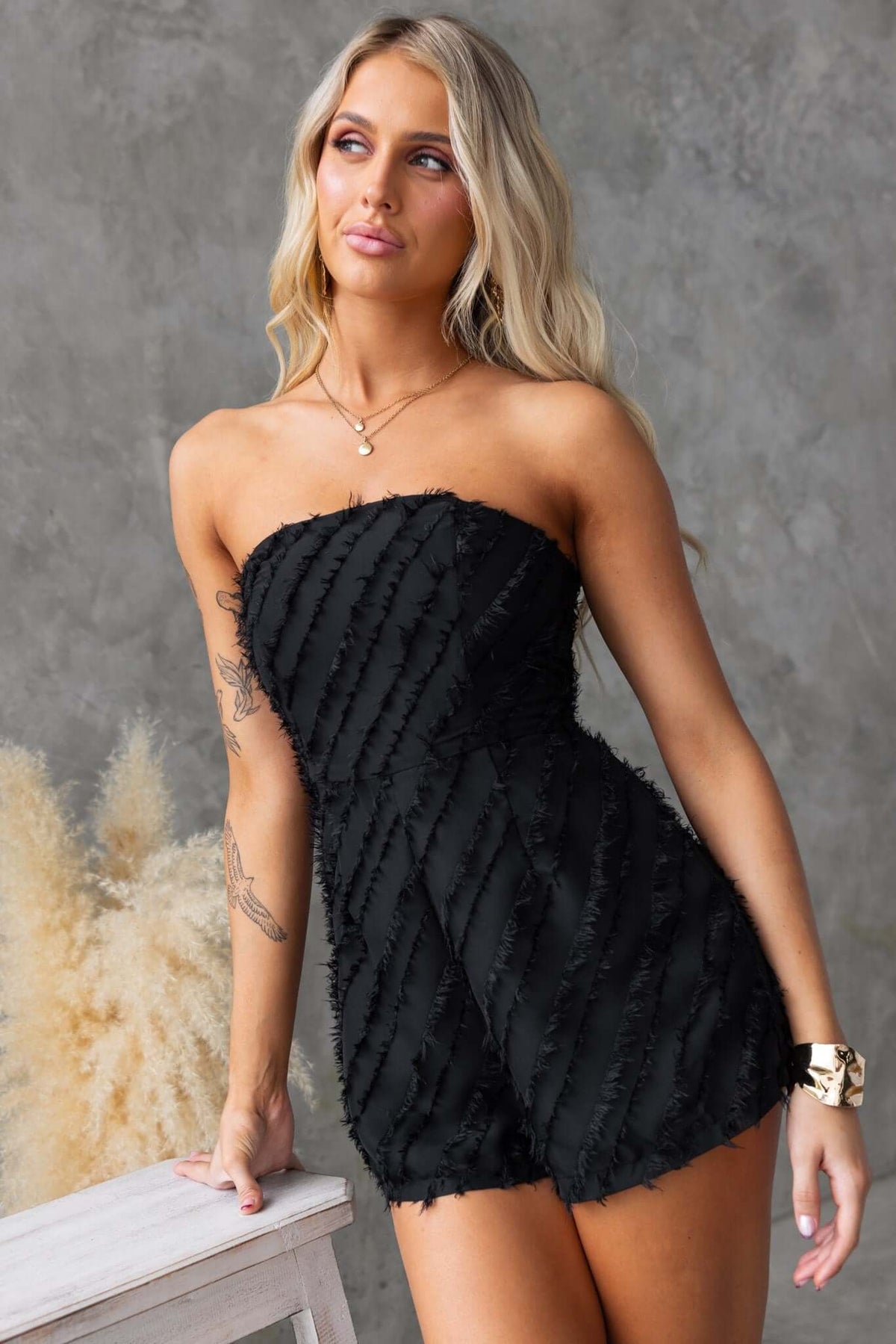 Model wearing a black strapless Bossier playsuit with boning and textured material, styled elegantly.