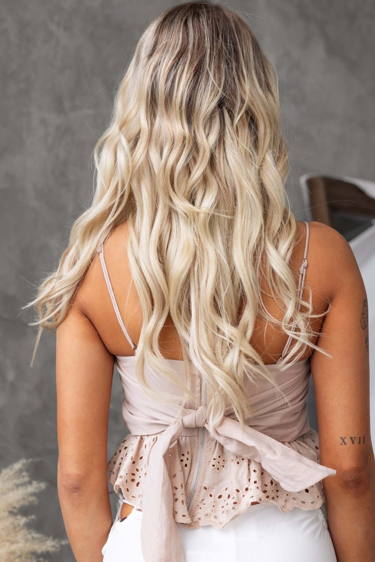 Back view of a woman wearing a light pink Adams top with adjustable straps and a tied waist detail.
