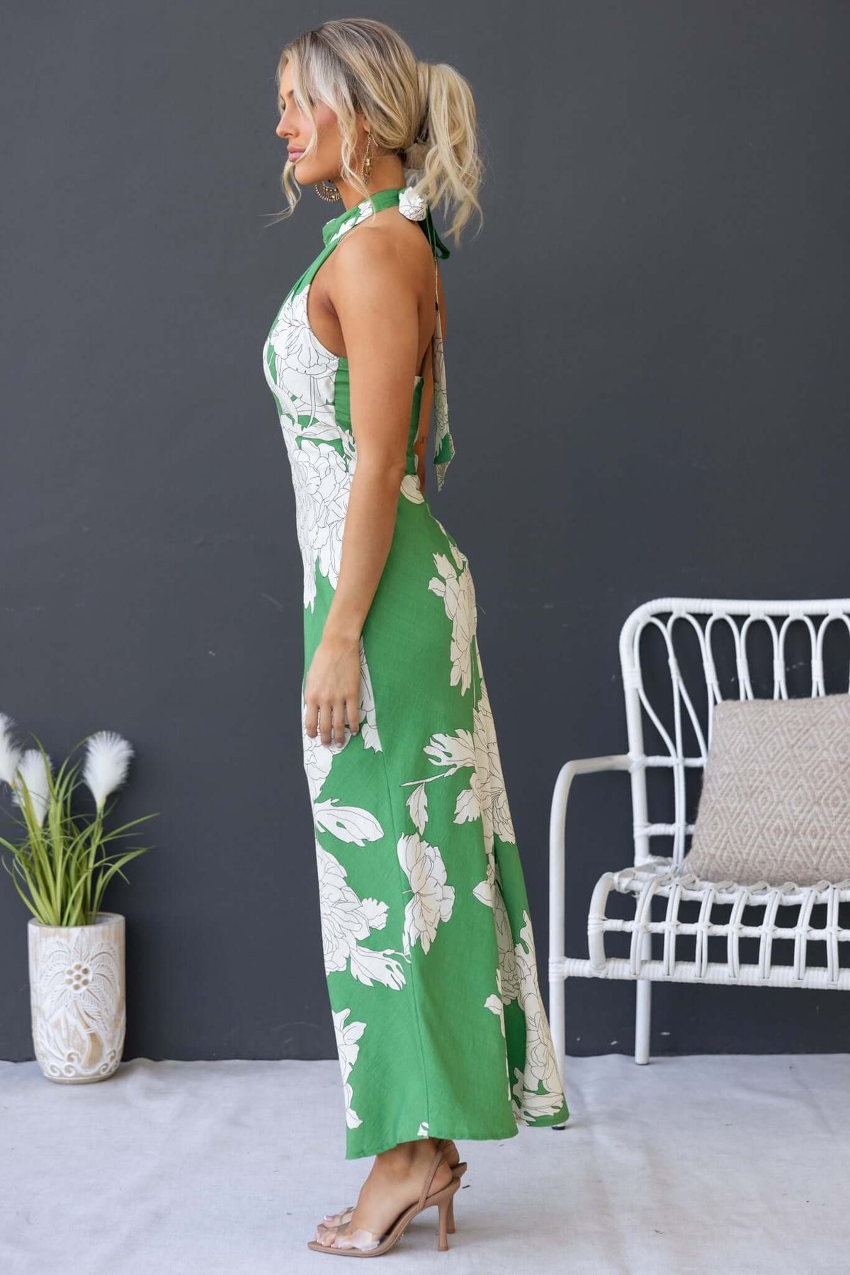 Model wearing the Forbidden Love Maxi Dress with a high tie neckline and floral pattern in green, showcasing a side view.