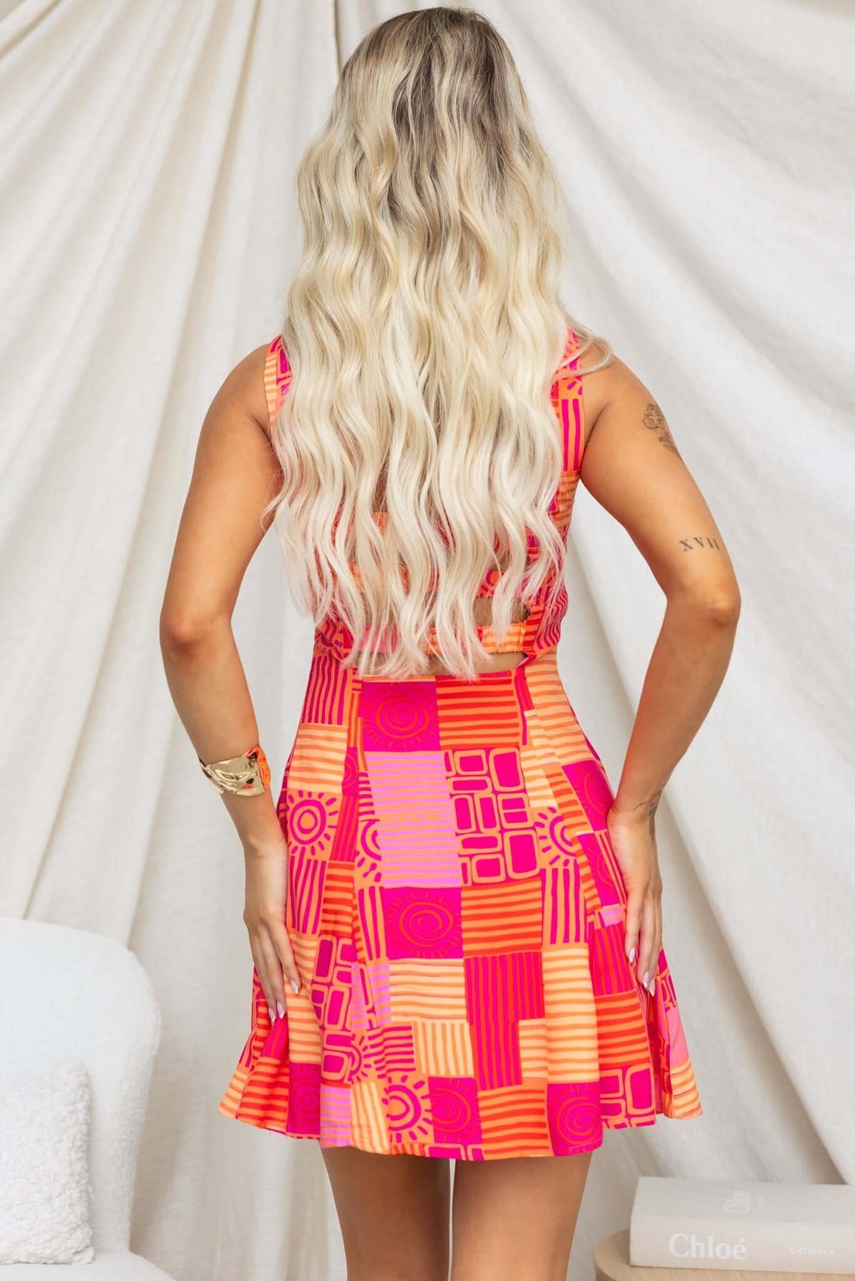 Back view of a model wearing a vibrant pink and orange patterned dress with a flared skirt.
