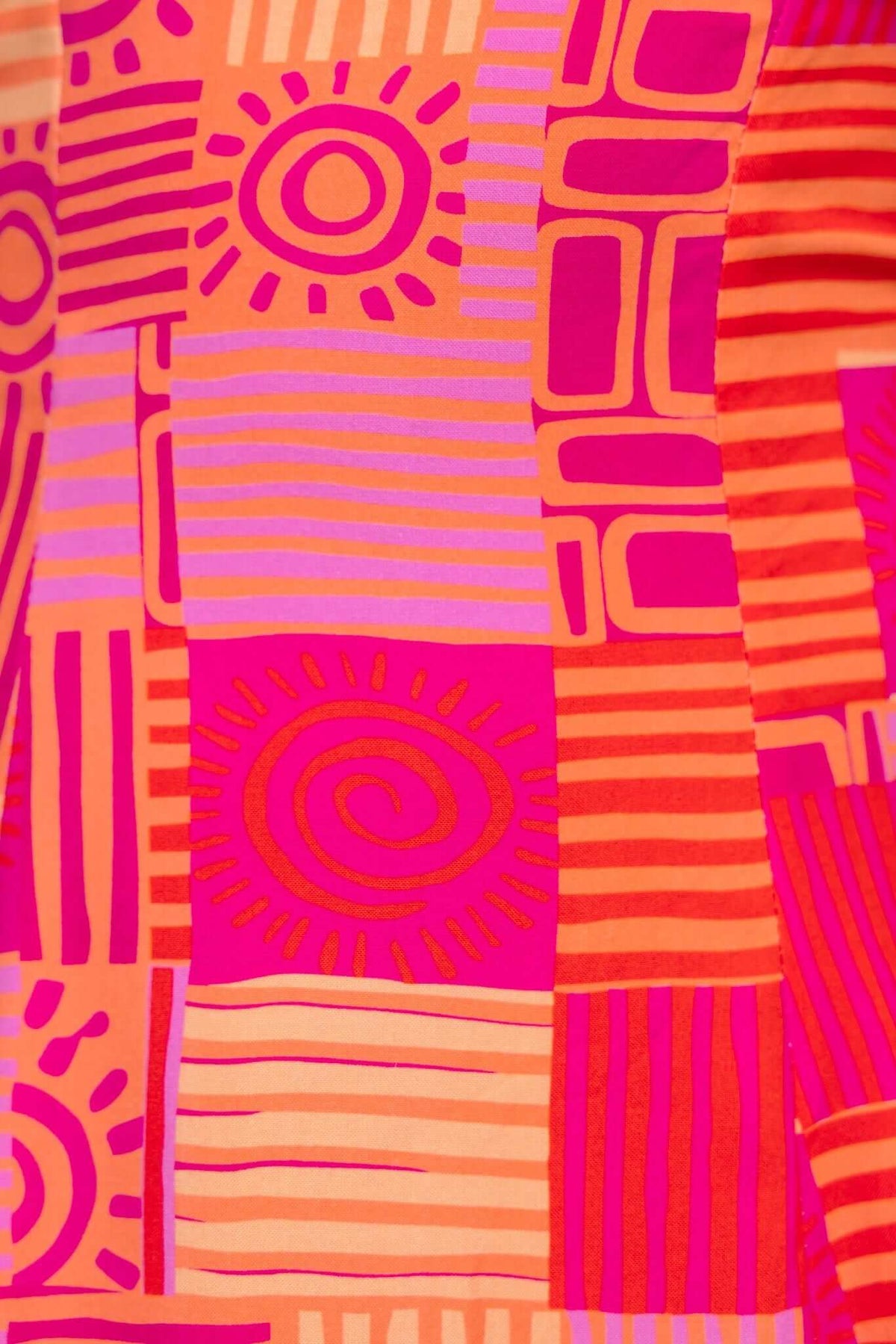 Close-up of vibrant pink and orange patterned fabric featuring sunny motifs and stripes, ideal for stylish summer dresses.