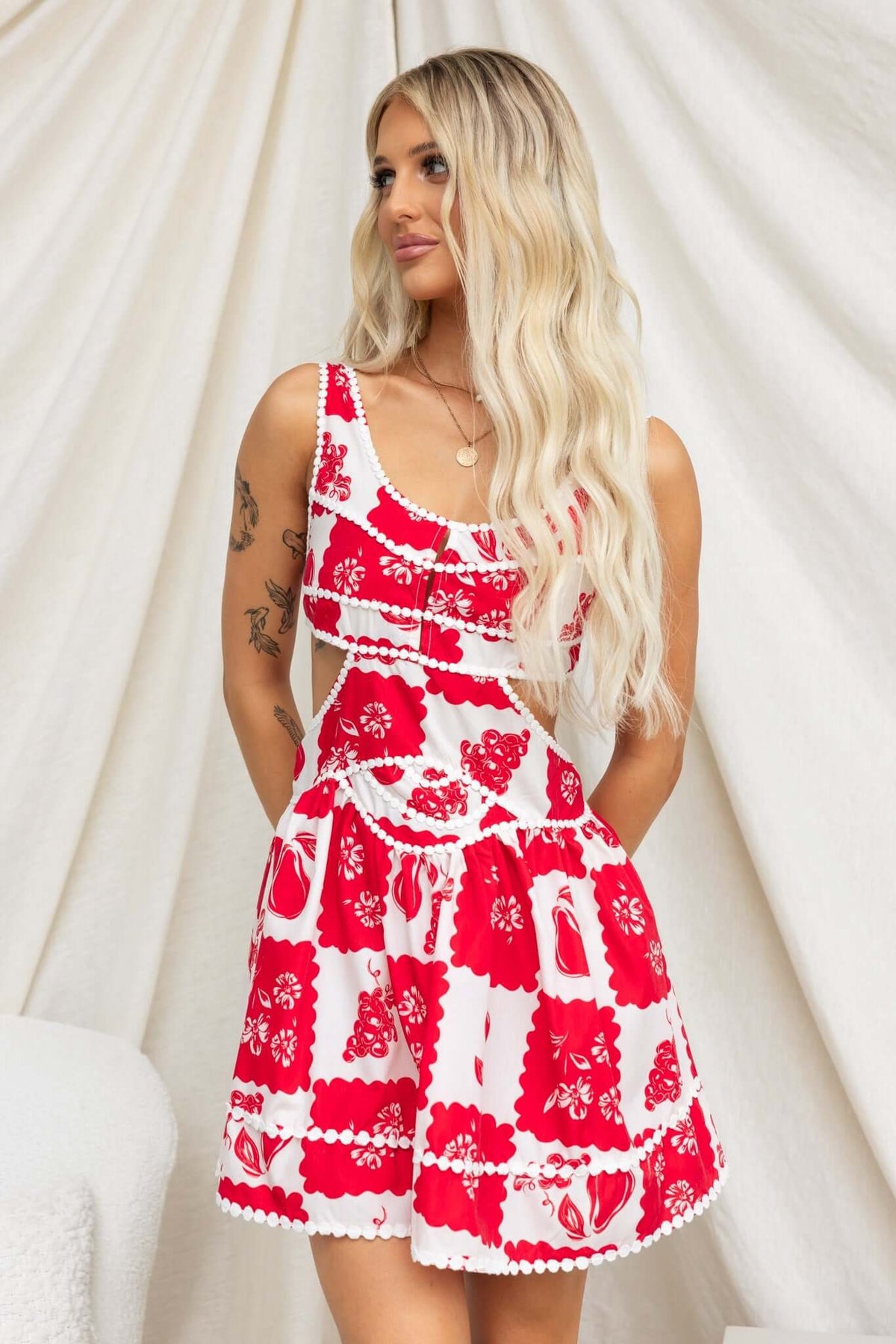 Model wearing Inara Dress, a red floral print dress with adjustable straps and cut-out at the waist, styled elegantly.