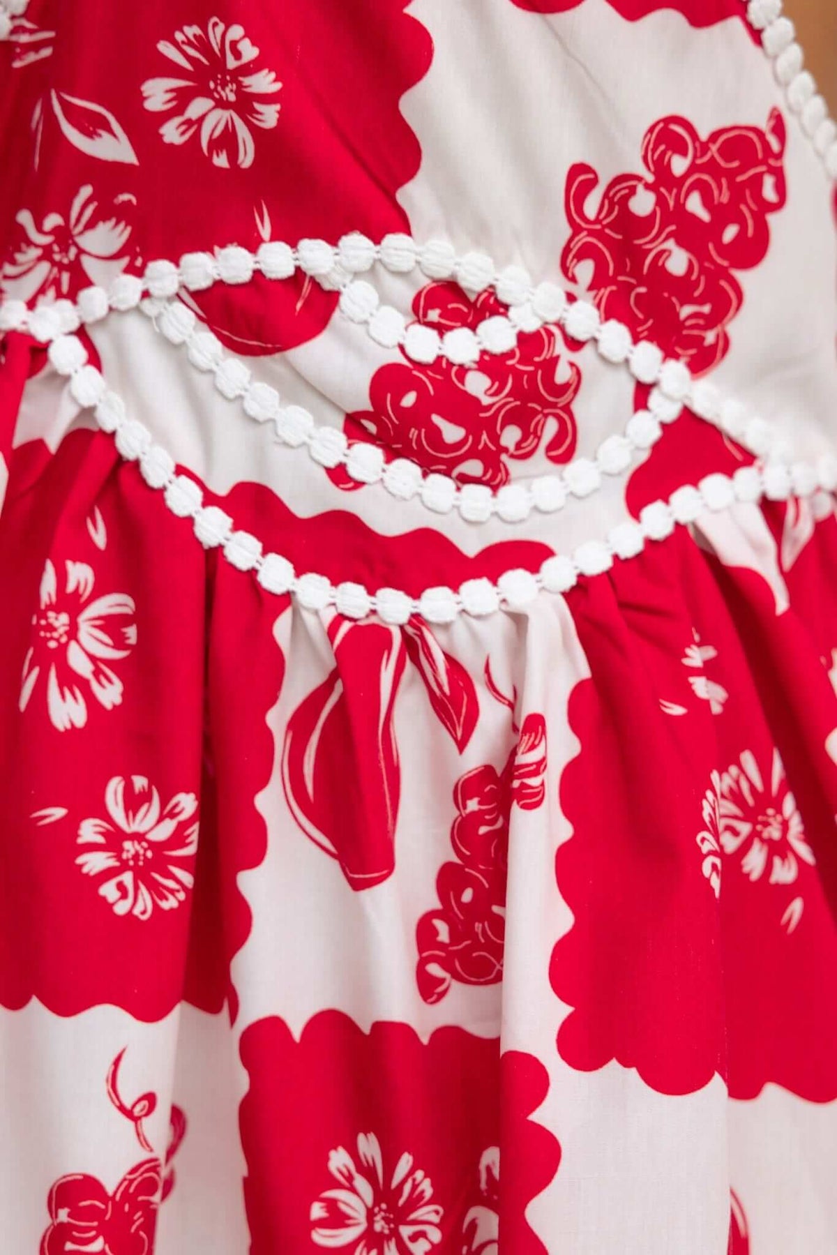 Close-up of Inara Dress showing red floral pattern with white trim detail, featuring adjustable straps and cut-out at waist.