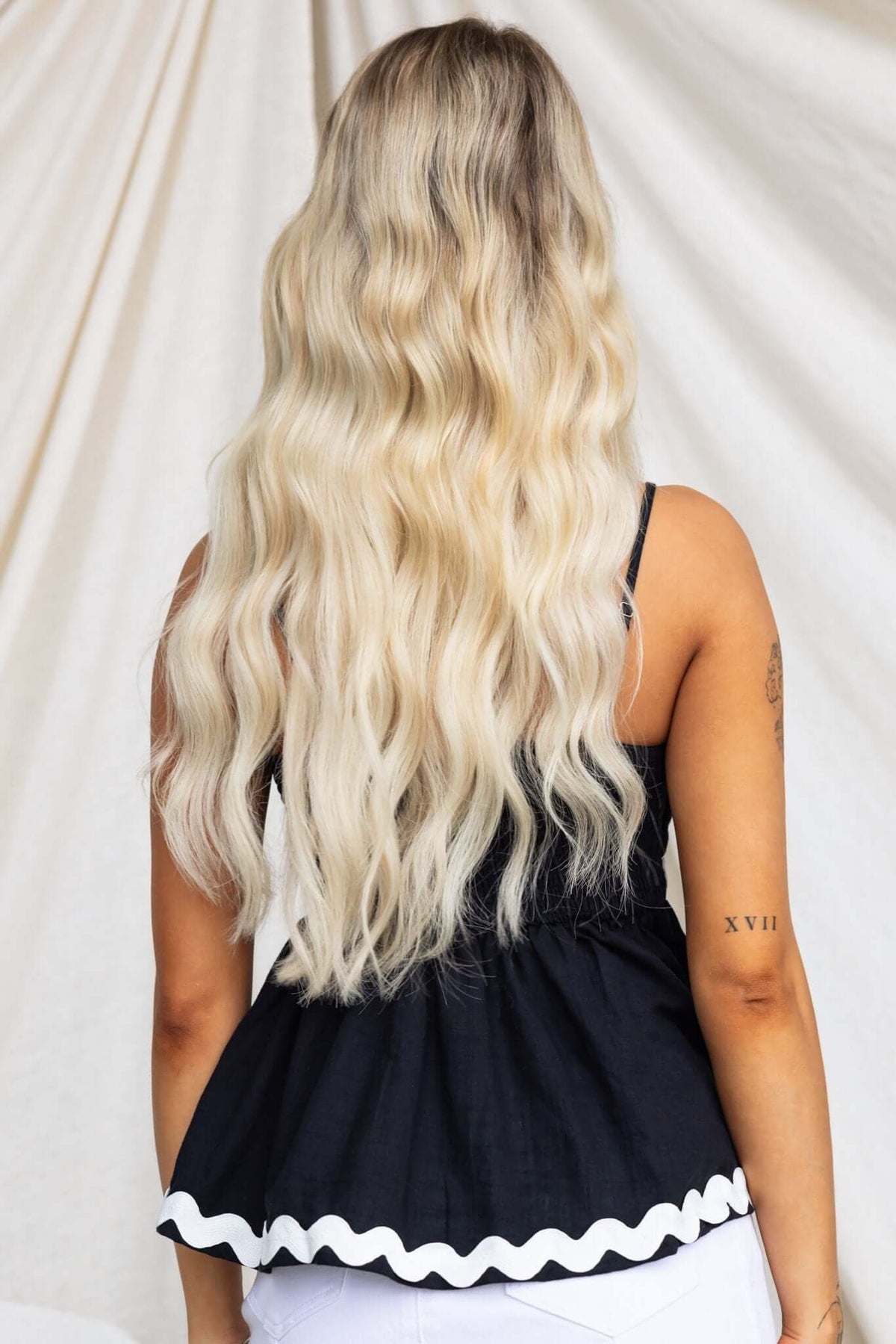 Back view of a woman wearing the black Ursley top with adjustable straps and ruffled hem, showcasing long wavy hair.