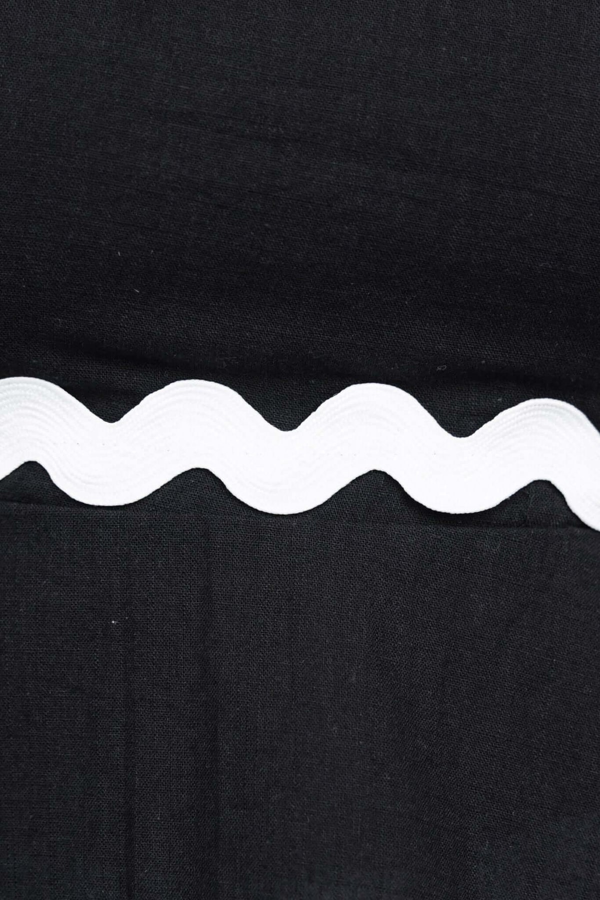 Close-up of black fabric featuring white wavy trim detail, highlighting the stitching of the Ursley Top.