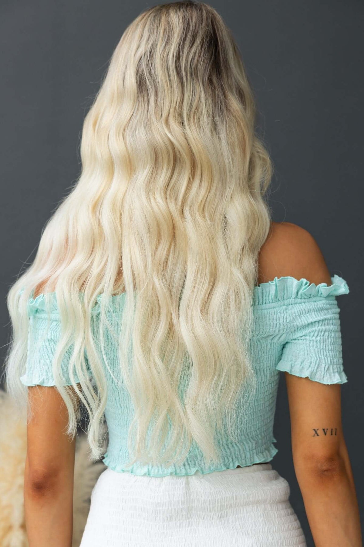 Back view of a woman in a mint green elastic top with wavy hair, showcasing a modern, stylish outfit.