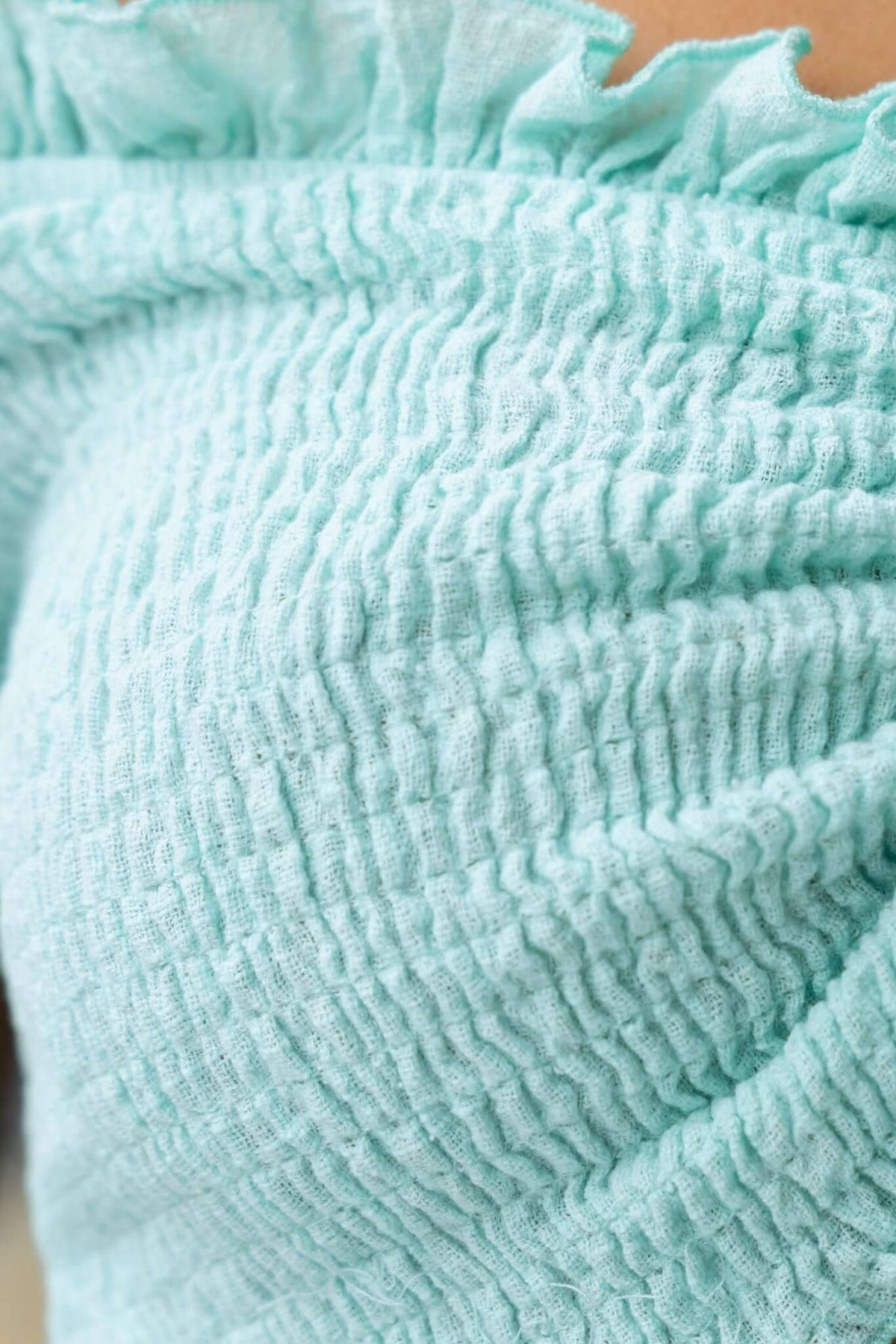 Close-up of the textured mint green fabric of the Vitora Top featuring stretchy smocking and ruffled details.