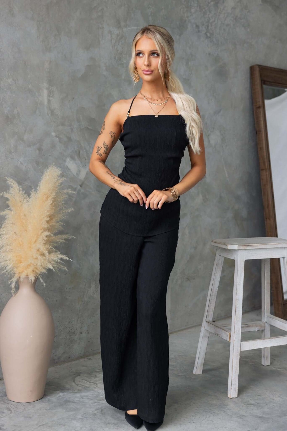 Stylish woman in black Kayce Set, featuring tie neckline and mid-high waist pants, posed elegantly against a modern backdrop.