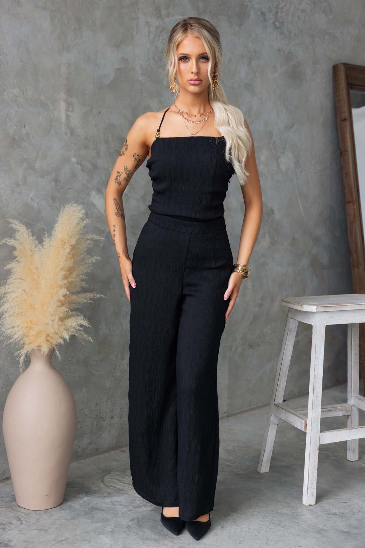 Model wearing Kayce Set, a black two-piece outfit with a tie neckline and mid-high waist pants, styled against a neutral background.