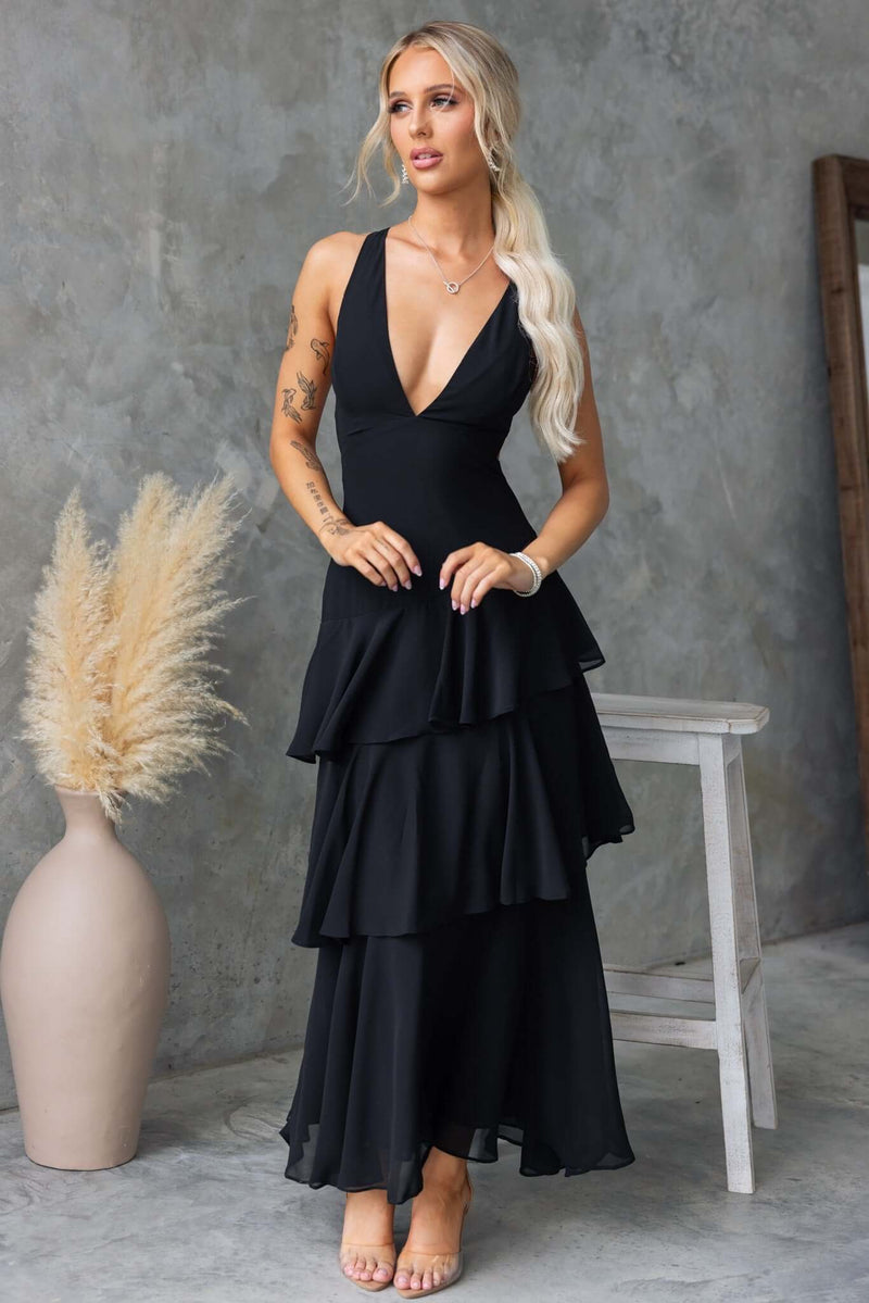 Stylish woman in a black maxi dress featuring a V-neckline and multi-tier ruffle hem, perfect for elegant occasions.