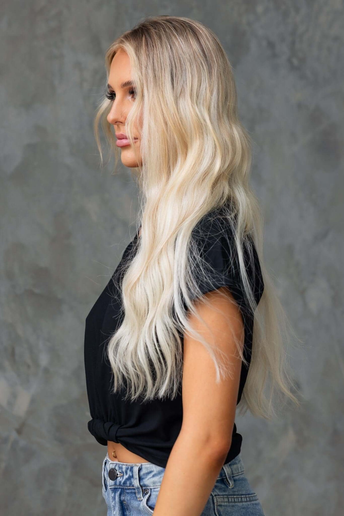 Model showcasing the Mell Tee with V-neckline and twist hem, styled with ripped jeans and flowing blonde hair.