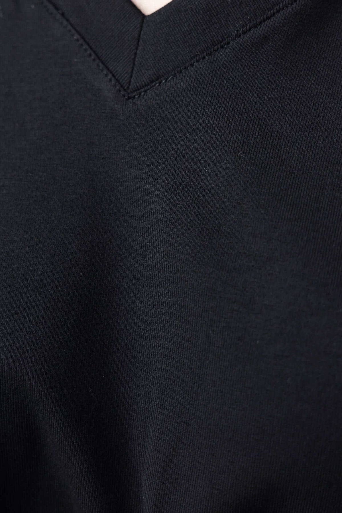 Close-up of Mell Tee's V-neckline in black fabric, showcasing soft stretch material and detailed stitching.