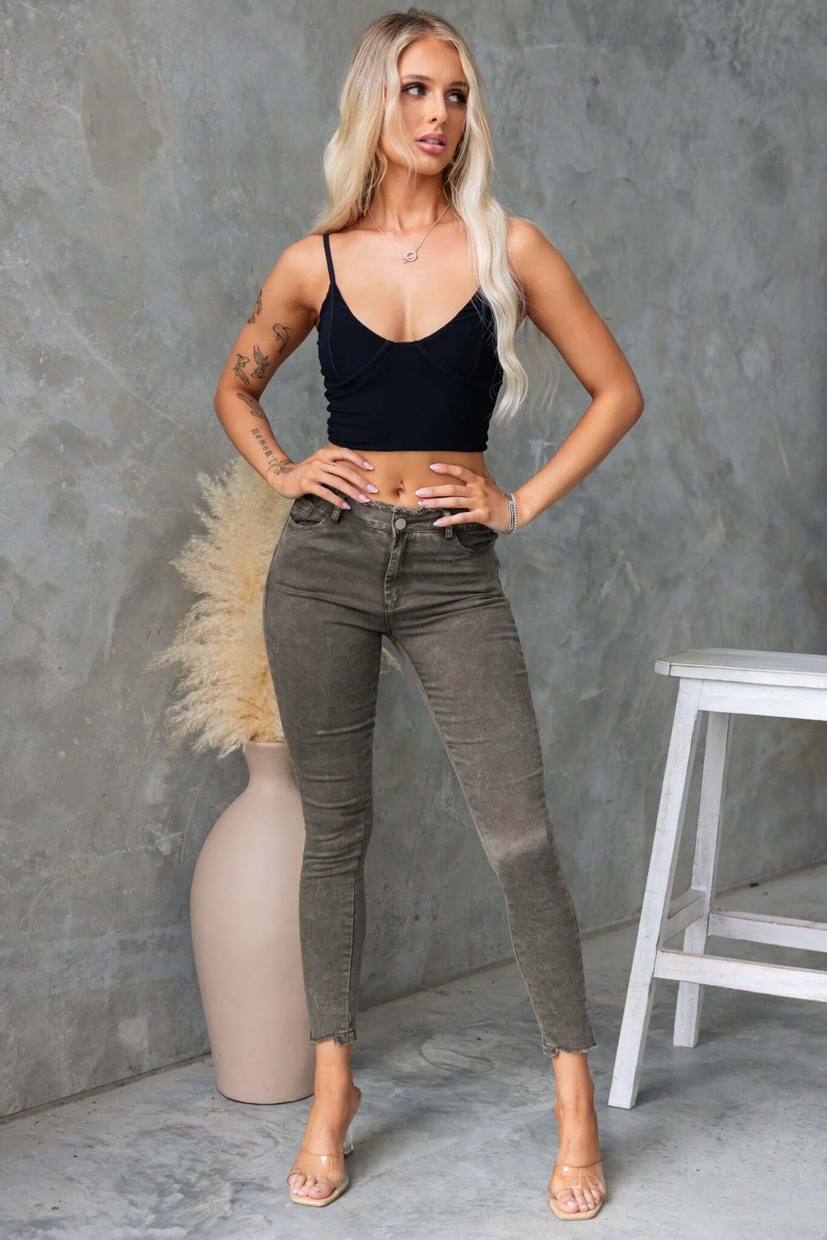 Woman in black crop top wearing Cassander Jeans with frayed edges, posing against a textured background.