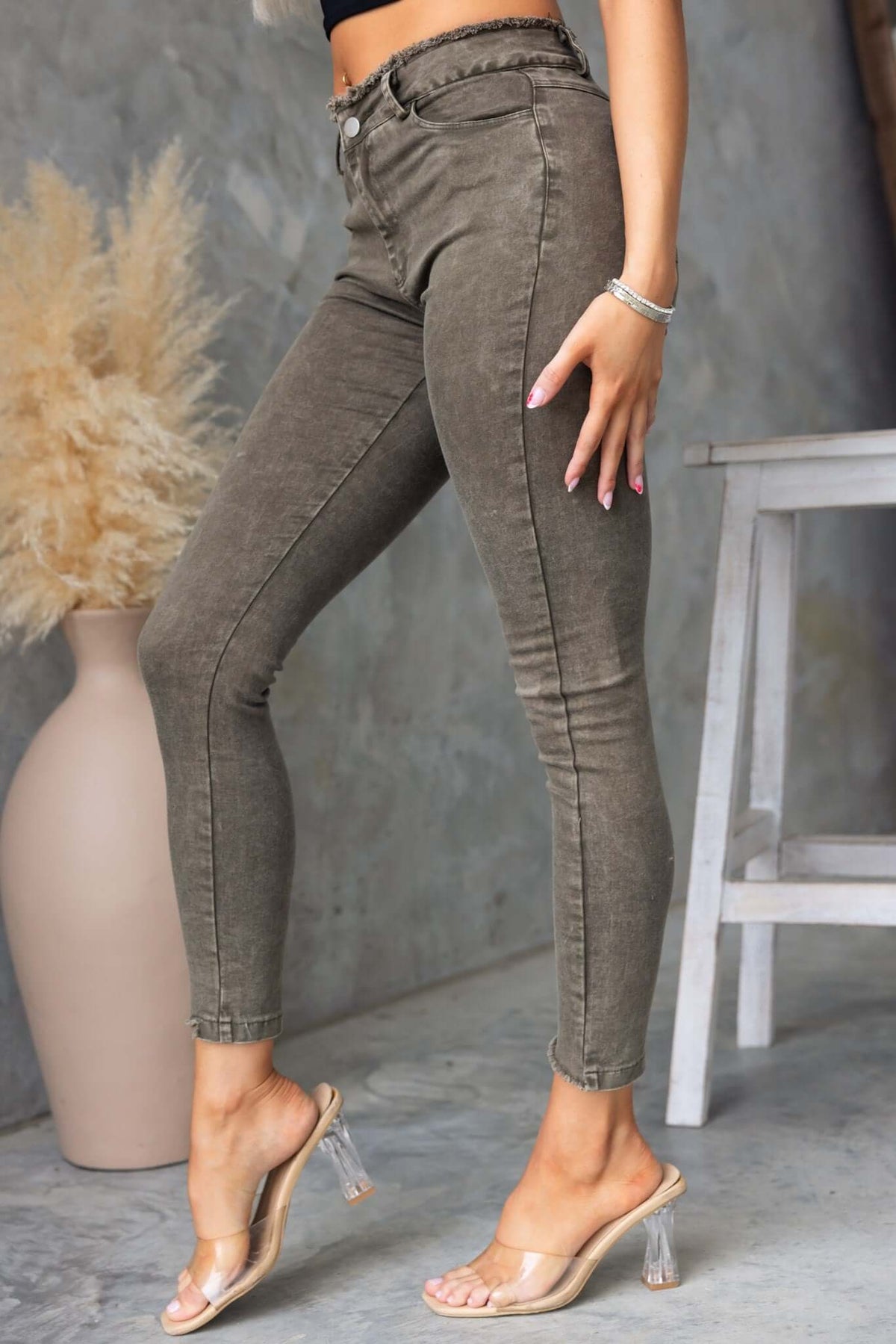 Model showcasing Cassander Jeans with frayed cuffs, mid-high waist, and stretch material in an olive green color.