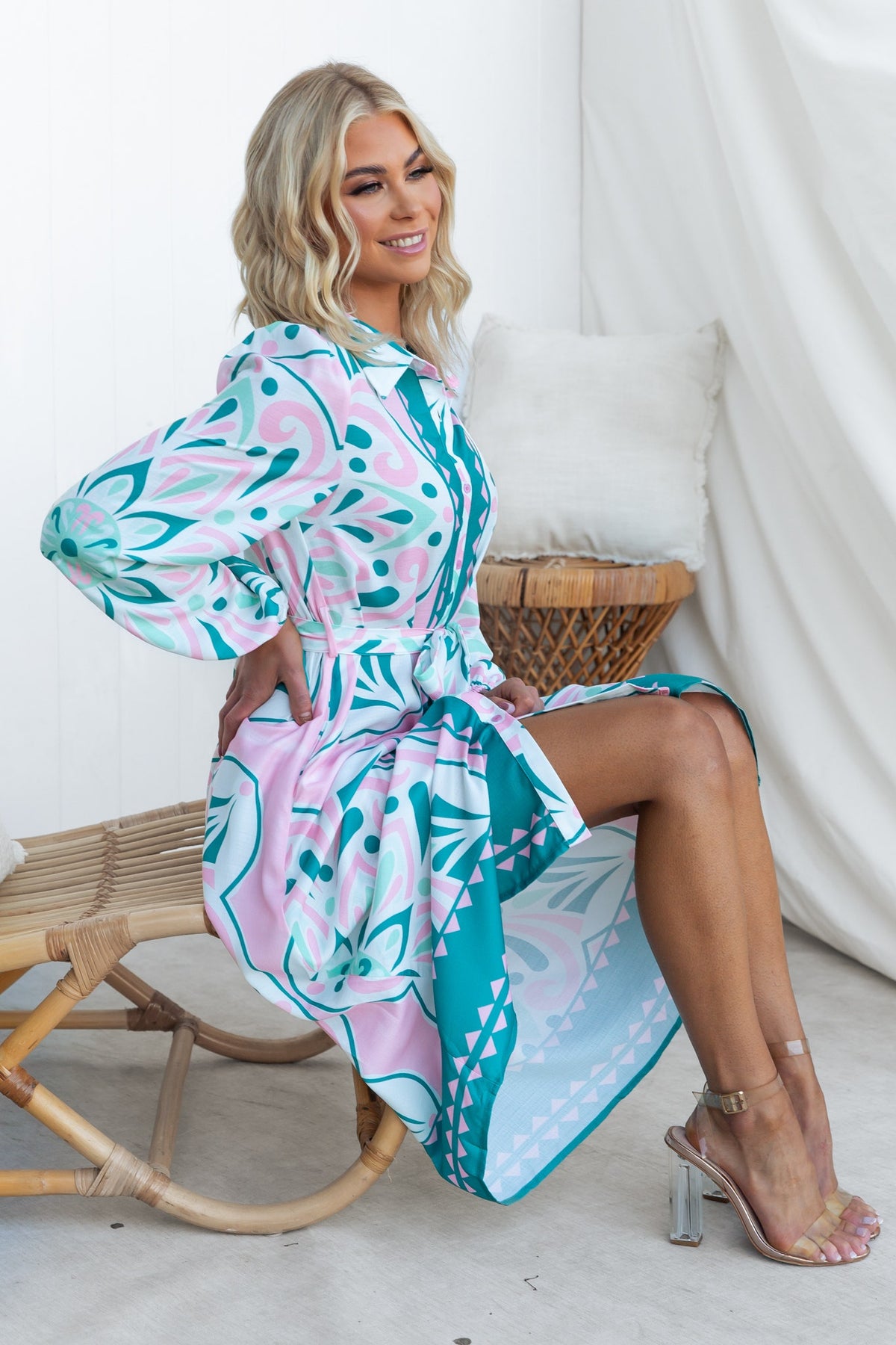 Model wearing the Faenza Midi Dress with a colorful floral design, sitting on a chair, showcasing the dress's style and fit.